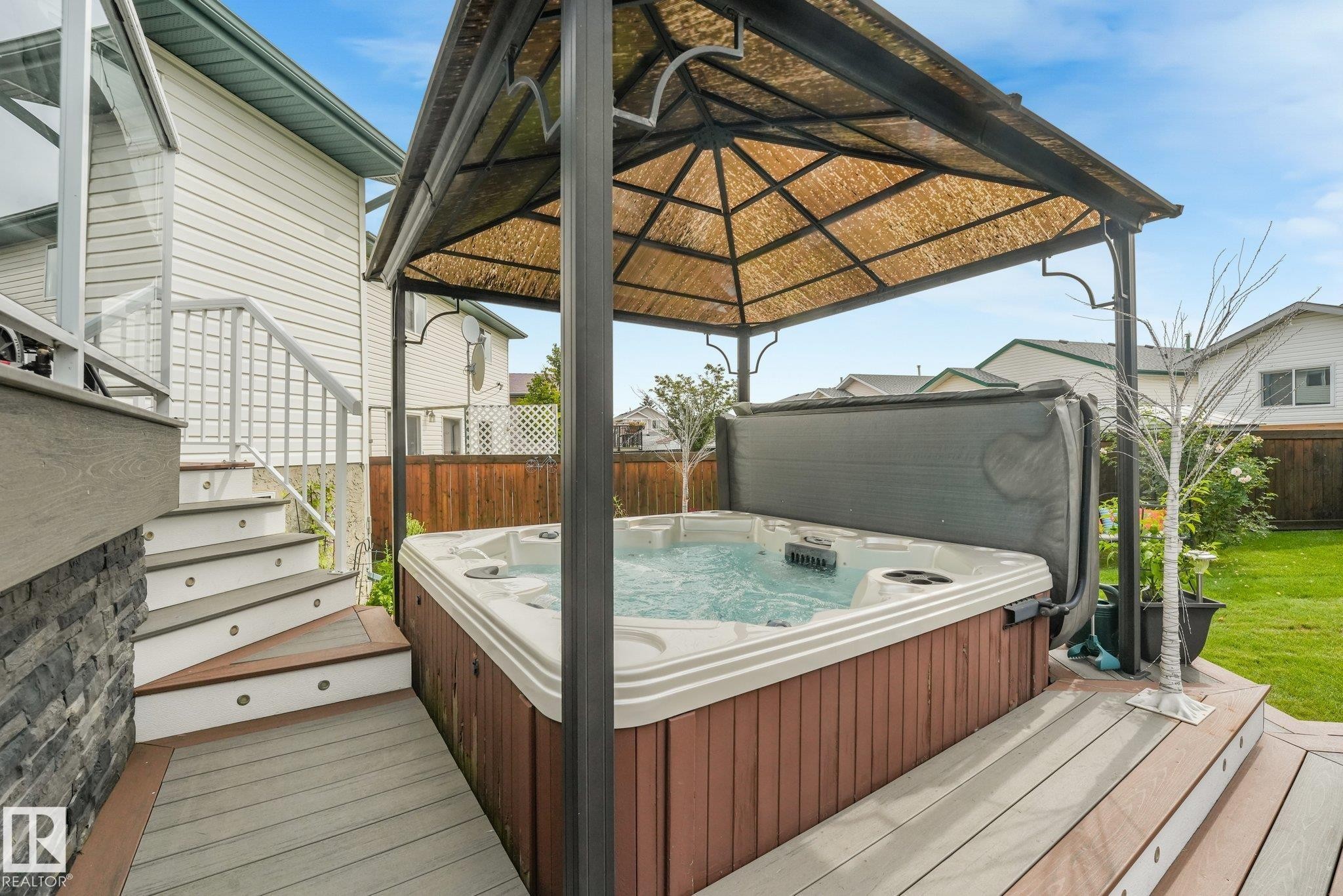 Built-in hot tub with a metal gazebo, composite deck, stone veneer accent wall, and integrated stair lighting - 12827 150 Avenue Nw, Edmonton, AB