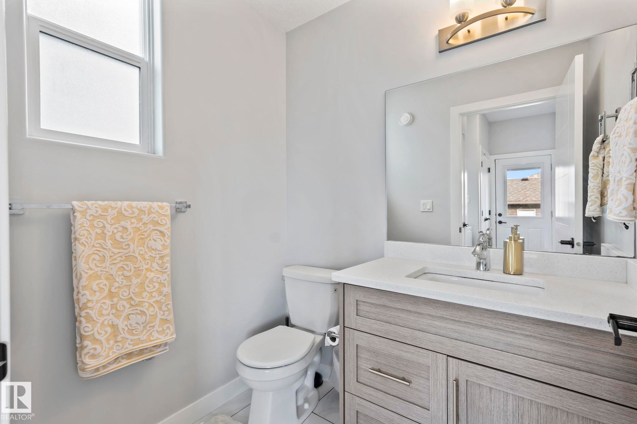 Bathroom featuring a light wood-finish vanity with an integrated sink, white countertop, and contemporary wall-mounted light fixture - 10338 162St Nw, Edmonton, AB