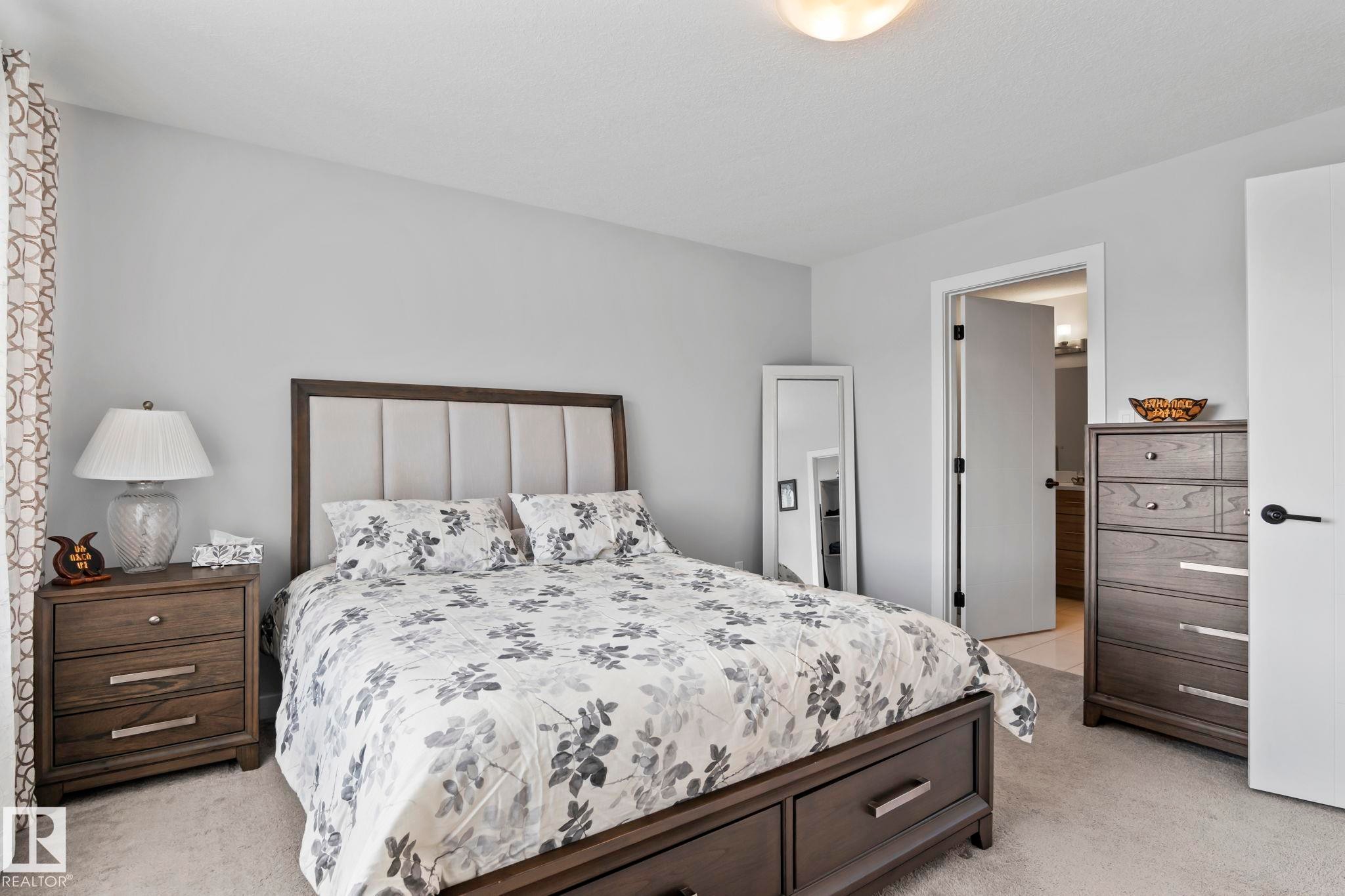 Neutral wall color, soft carpeting, recessed panel headboard, dark wood-finish nightstand, built-in ceiling light fixture - 10338 162St Nw, Edmonton, AB