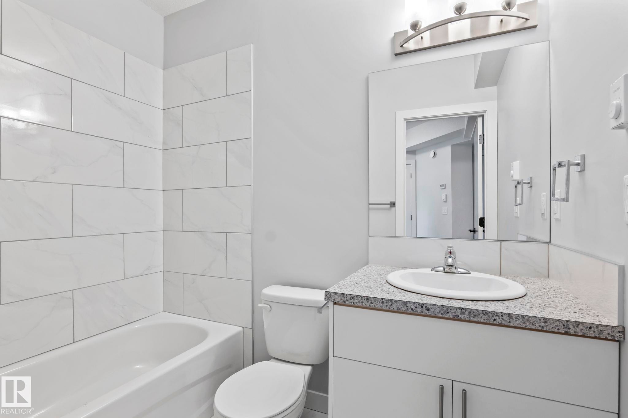 White tile tub surround, white vanity with integrated sink, laminate countertop, and brushed nickel hardware - 10338 162St Nw, Edmonton, AB