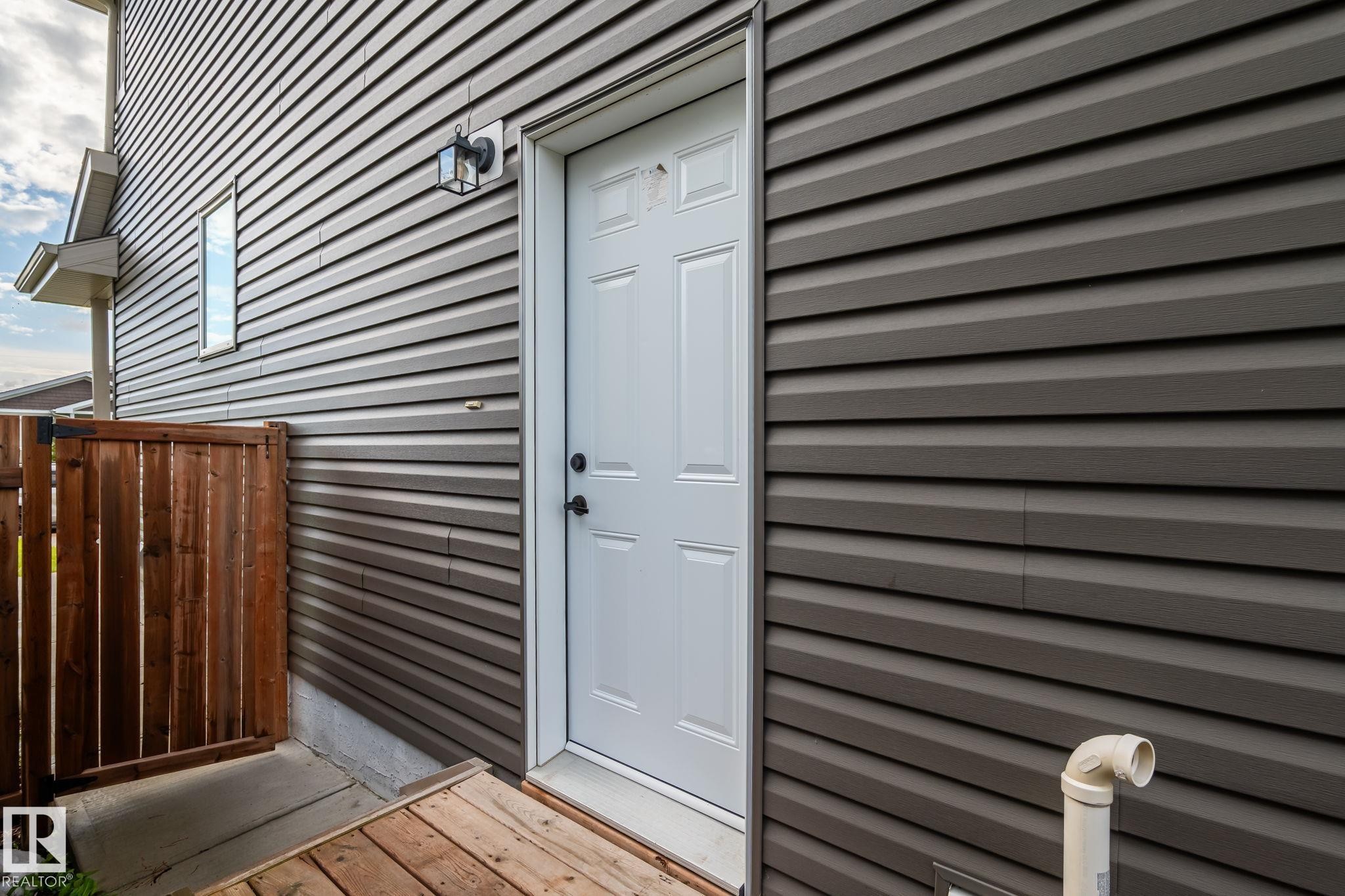 Brown horizontal siding with white trim, featuring a white paneled door with black hardware - 10338 162St Nw, Edmonton, AB