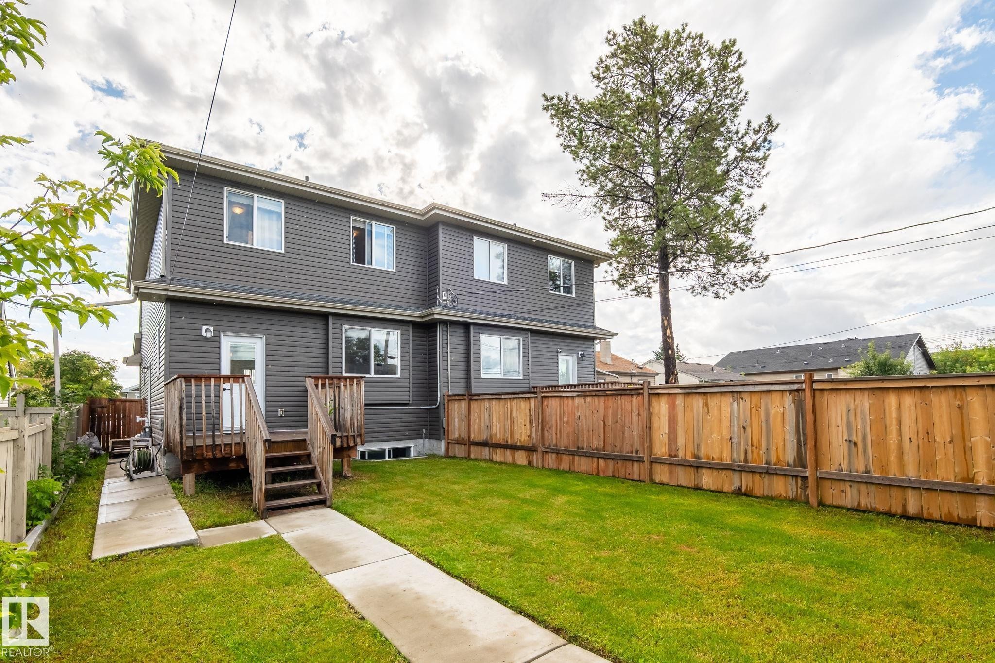 Expansive backyard featuring a manicured lawn, a wood deck with stairs, a privacy fence, and a concrete pathway - 10338 162St Nw, Edmonton, AB
