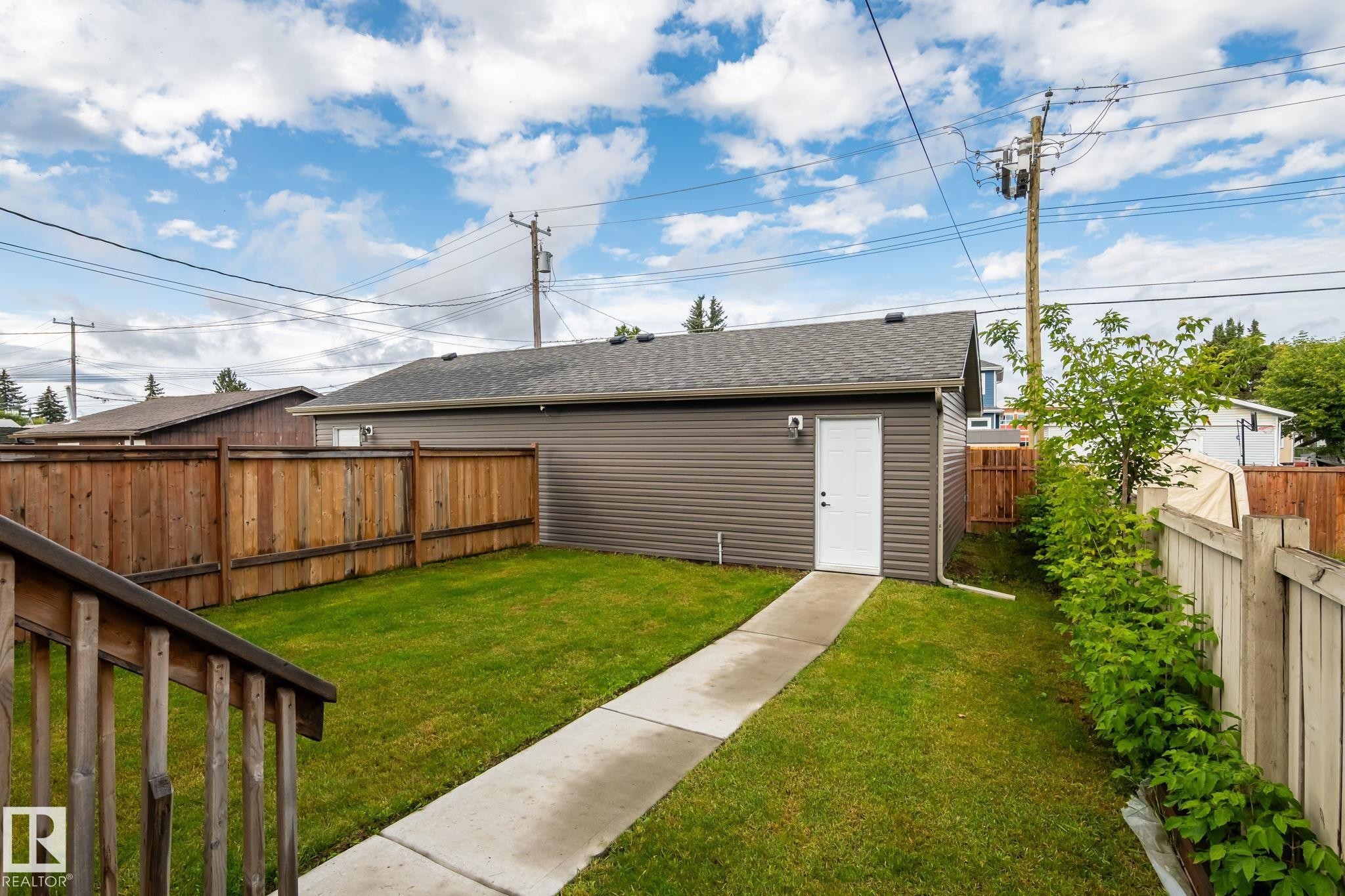 Detached garage with dark grey horizontal siding and a white side entry door - 10338 162St Nw, Edmonton, AB