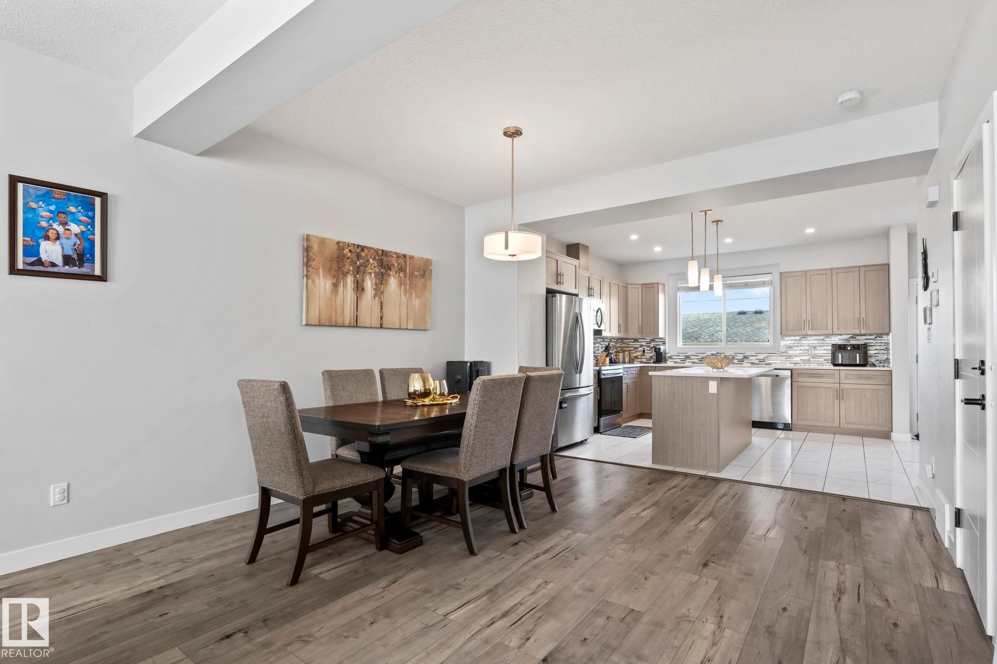 Wood-finish flooring throughout, with a recessed kitchen featuring a central island, light-toned cabinetry, and stainless steel appliances - 10338 162St Nw, Edmonton, AB