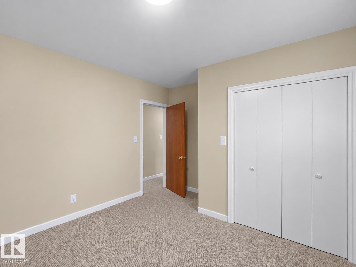 Neutral tone wall paint, light neutral carpeting, white trim, wood-finish interior door, and bi-fold closet doors - 12002 48 Street Nw, Edmonton, AB