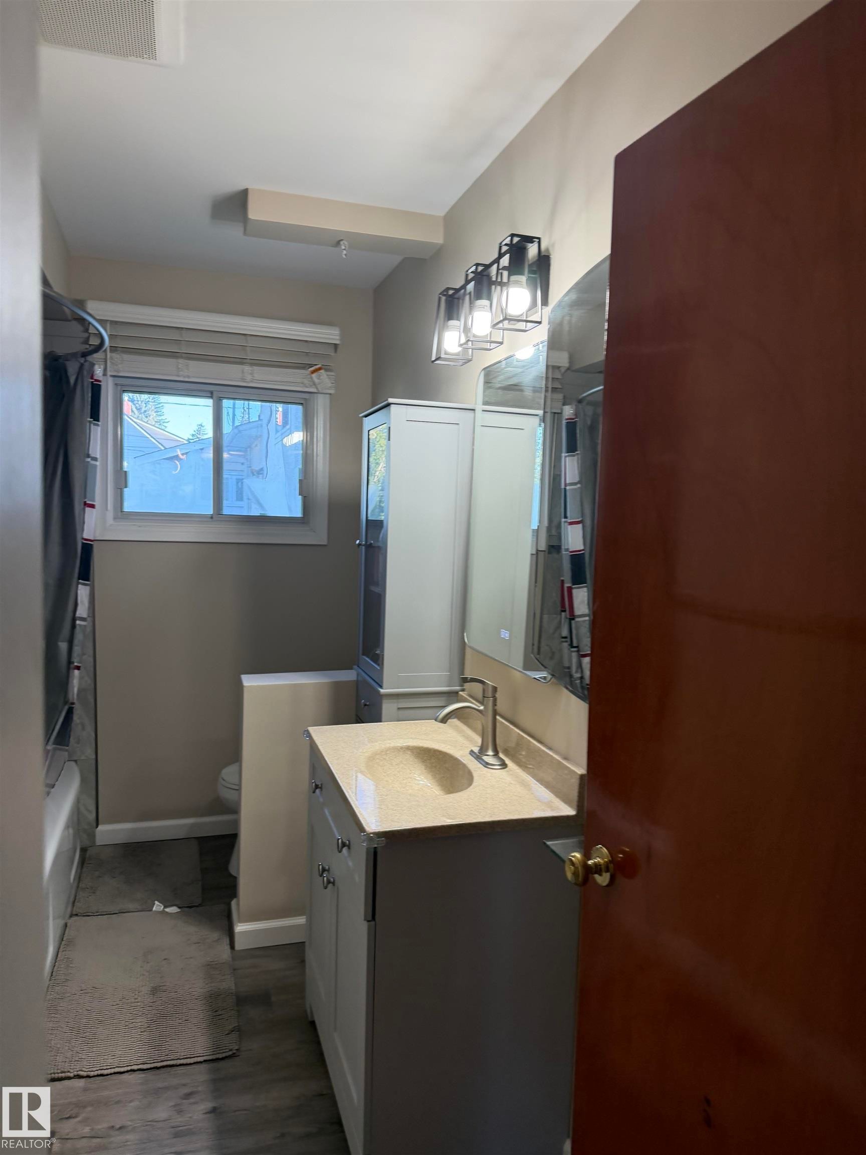 Vanity with a neutral countertop and single basin sink, framed mirror, and three-light vanity fixture - 12002 48 Street Nw, Edmonton, AB