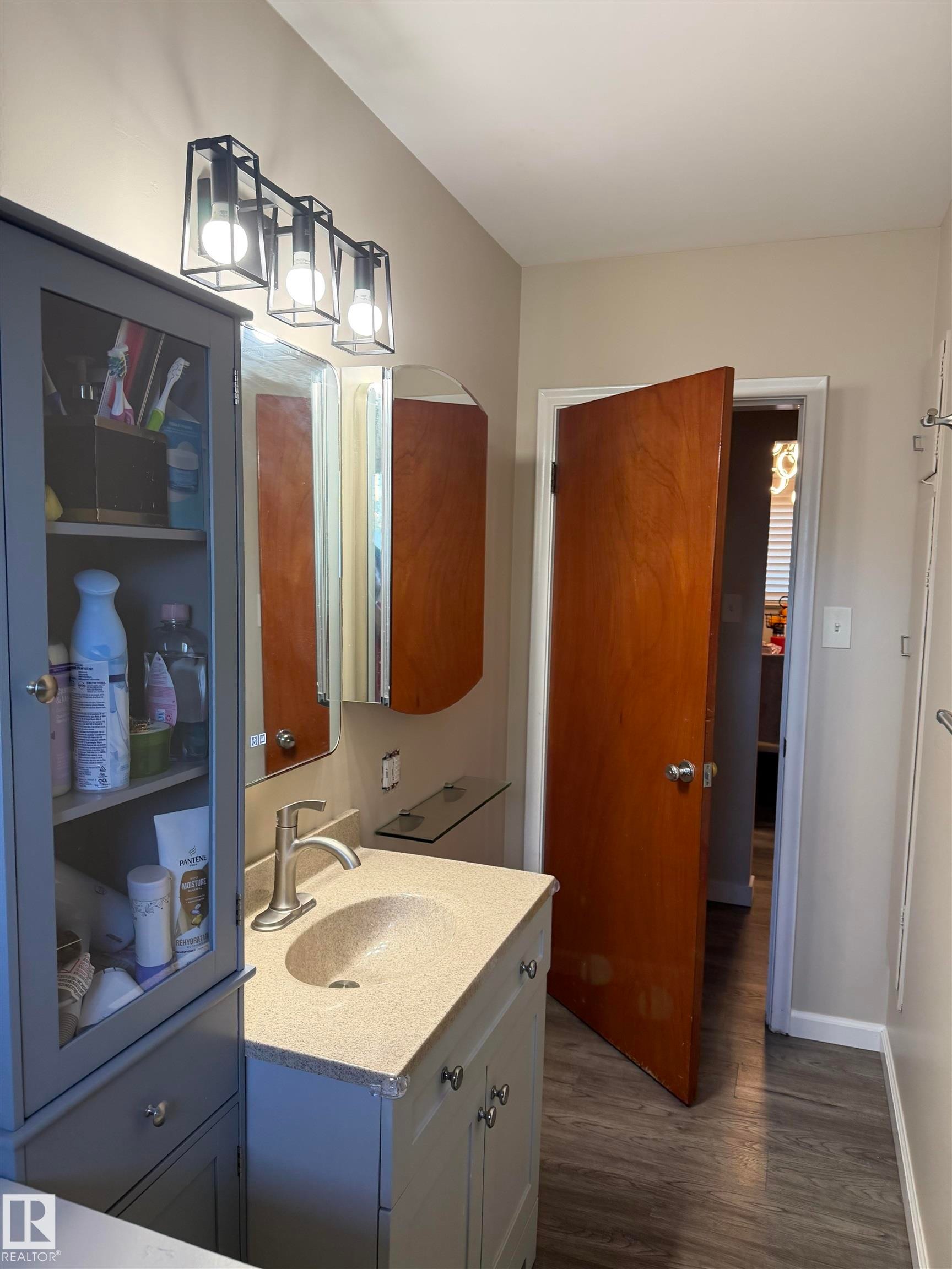 Vanity with integrated sink, modern wall-mounted light fixture, wood-finish flooring, and built-in medicine cabinet - 12002 48 Street Nw, Edmonton, AB