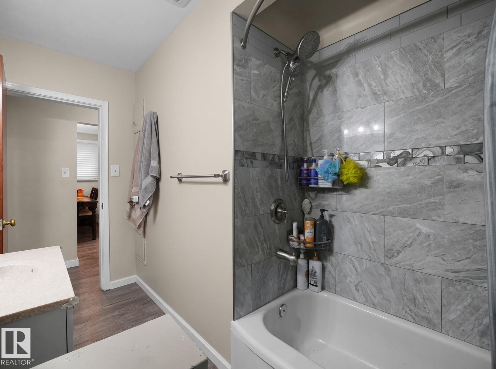Bathtub with tiled surround featuring a decorative accent band, chrome shower fixtures, and a vanity with a light-colored countertop - 12002 48 Street Nw, Edmonton, AB