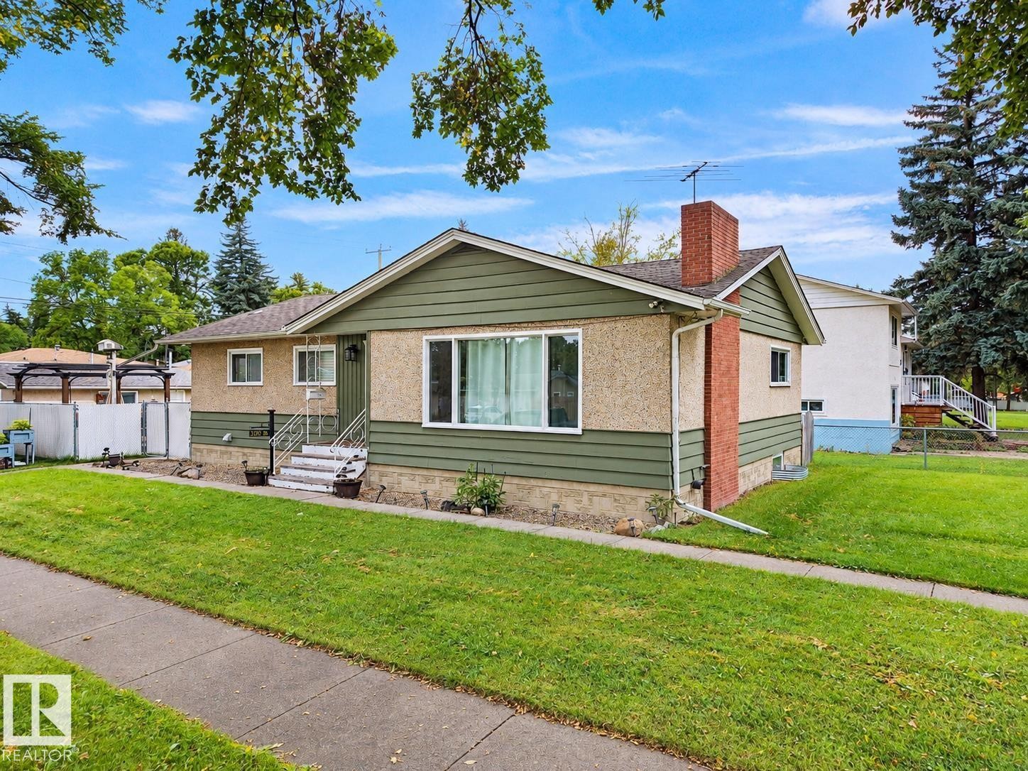 Exterior featuring green horizontal siding, stucco details, a brick chimney, and a concrete sidewalk - 12002 48 Street Nw, Edmonton, AB