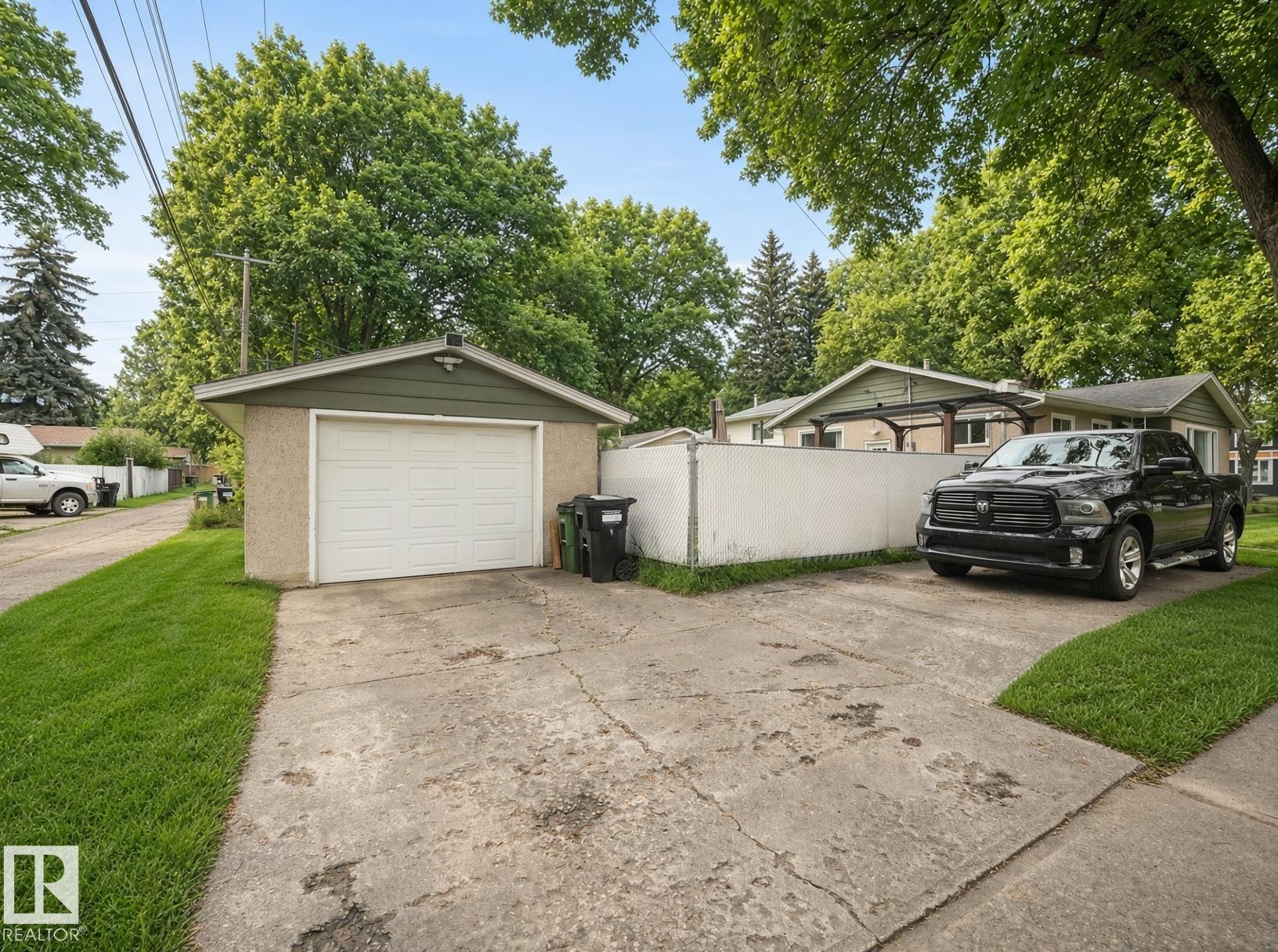 Detached garage with a white overhead door, concrete driveway, and a chain-link fence - 12002 48 Street Nw, Edmonton, AB