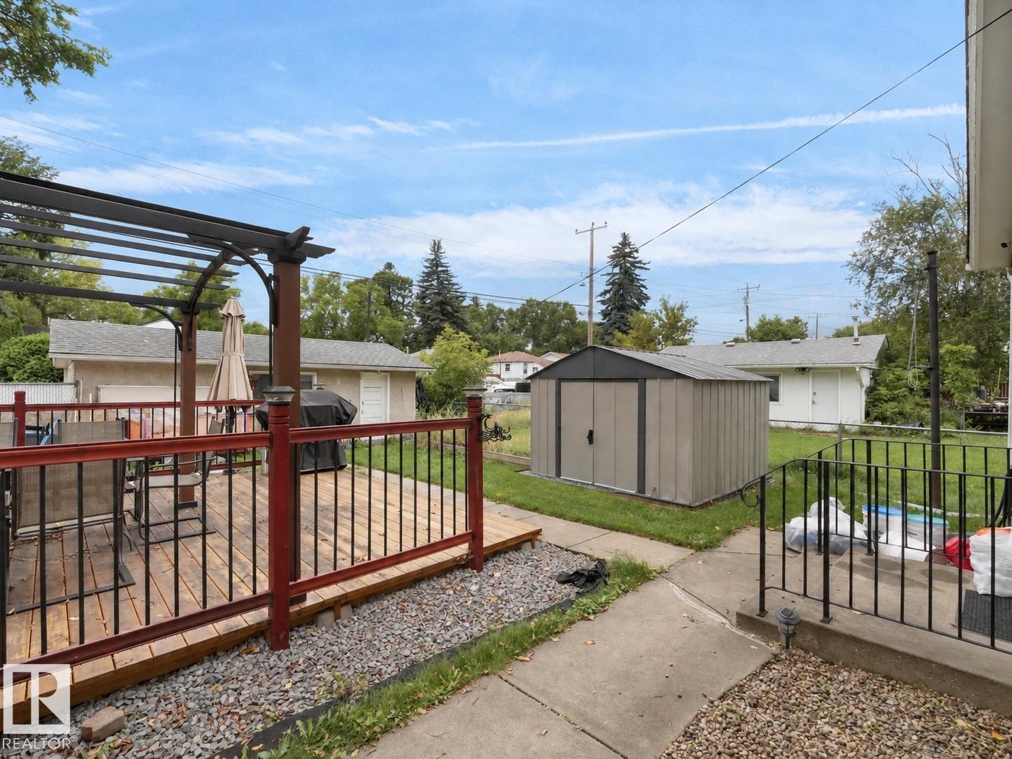 Expansive outdoor deck with wood flooring and red railing, featuring a metal pergola - 12002 48 Street Nw, Edmonton, AB