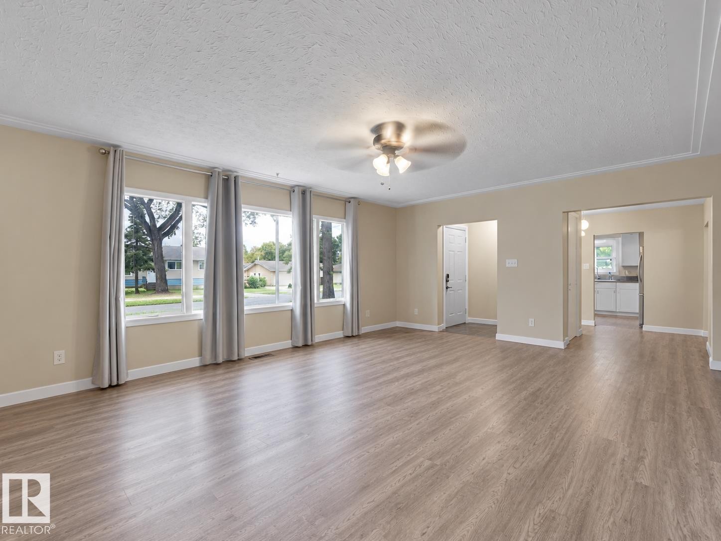 Expansive room featuring wood-finish flooring, multiple windows, a ceiling fan, and light-toned wall finishes - 12002 48 Street Nw, Edmonton, AB