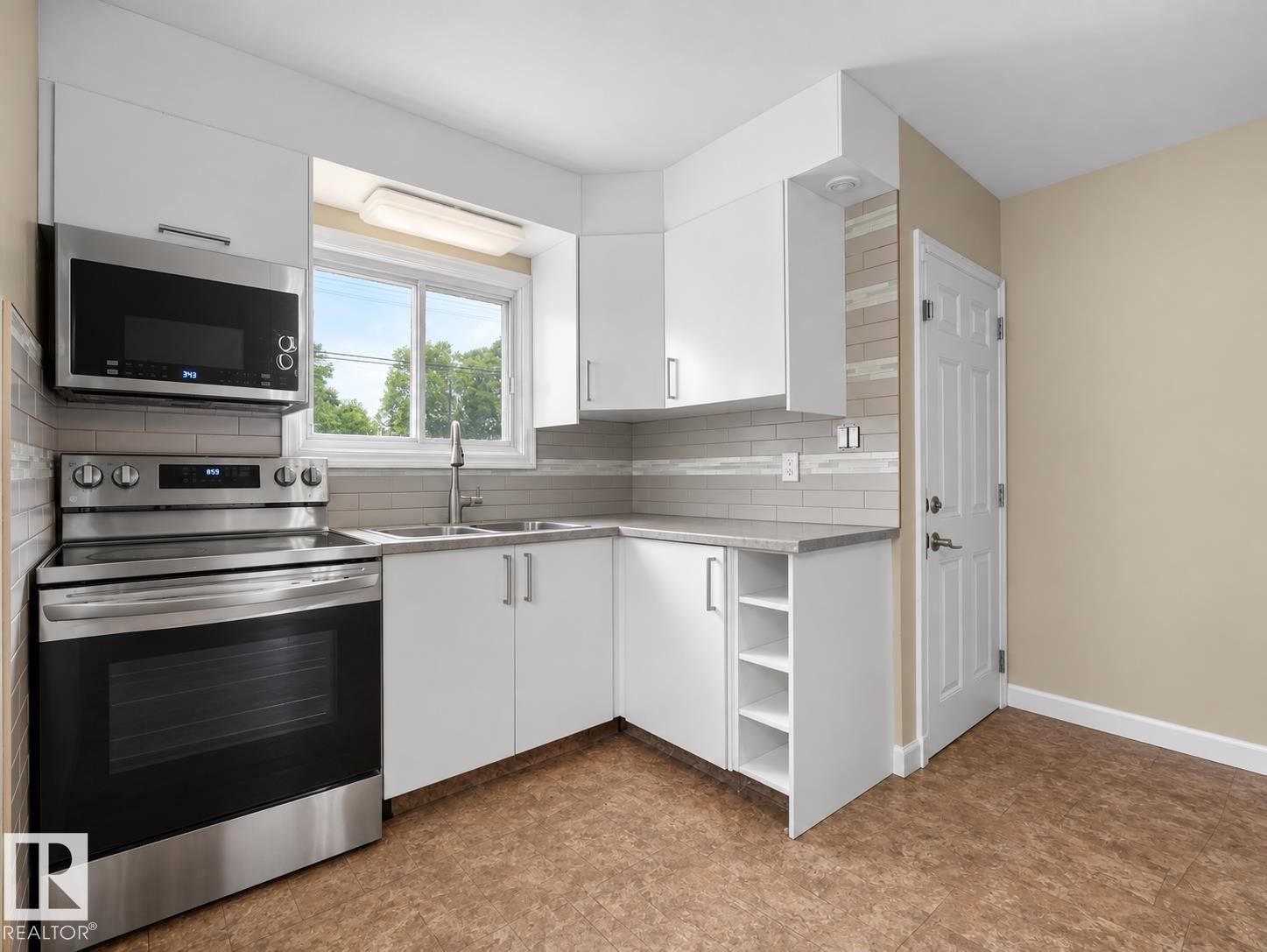 Contemporary kitchen featuring white cabinetry, stainless steel appliances, a tile backsplash, and durable flooring - 12002 48 Street Nw, Edmonton, AB