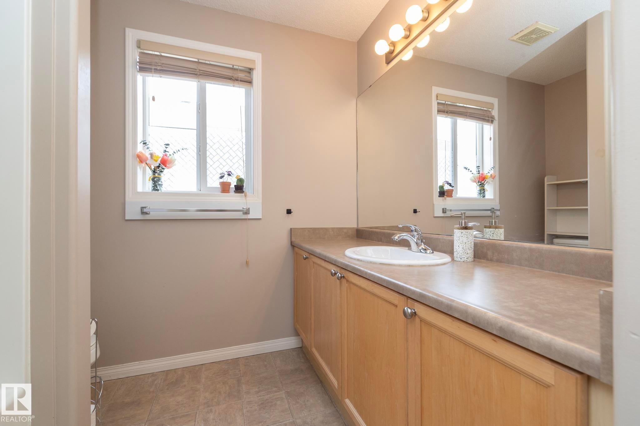 Bathroom featuring a light wood-finish vanity with an integrated sink, a large wall-mounted mirror, and overhead vanity lighting - 17908 89 Street Nw, Edmonton, AB - Indoor Photo Showing Bathroom