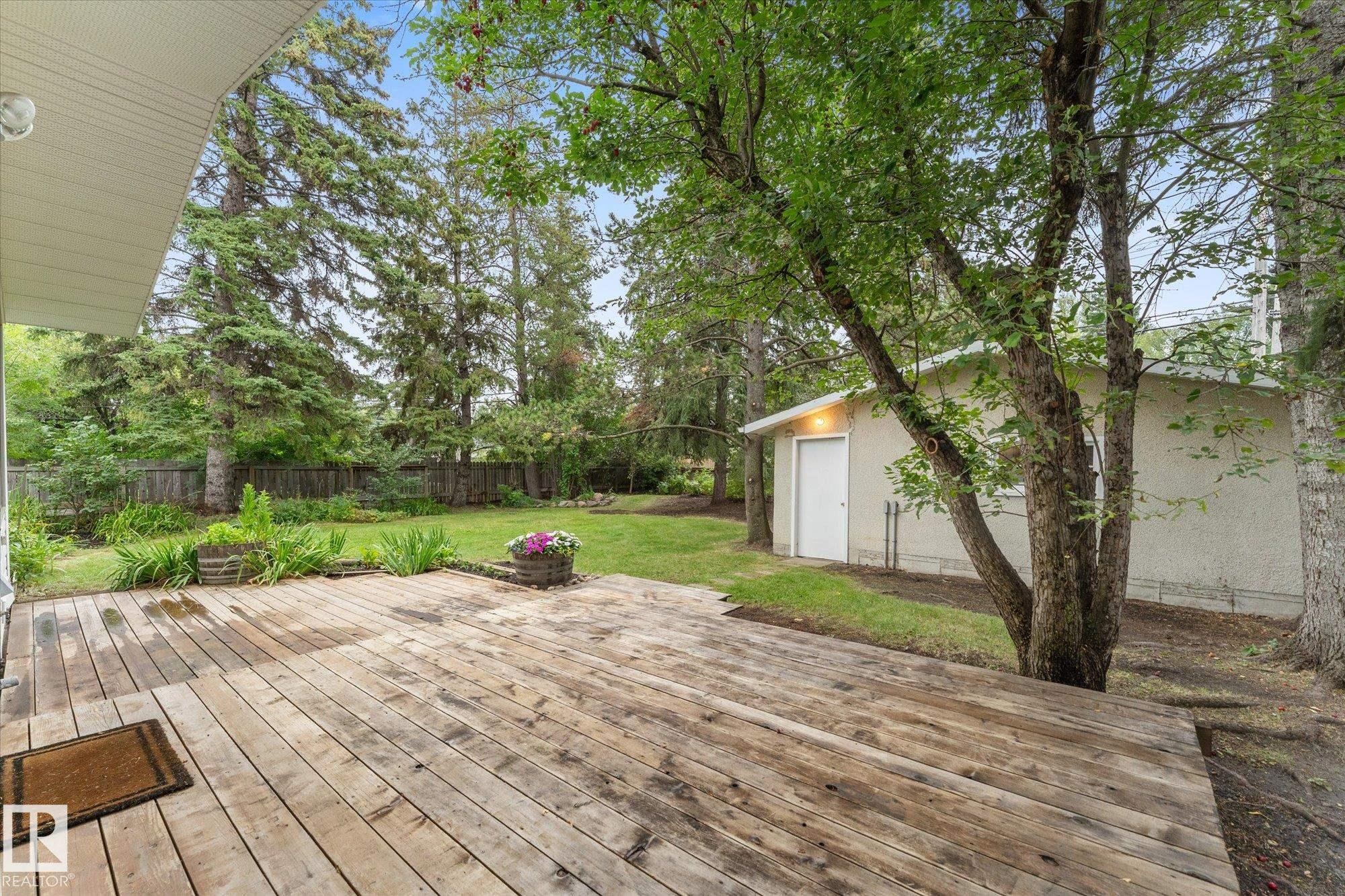 Expansive wood deck with a large manicured lawn, mature trees, and a detached building - 11311 Malmo Road Nw, Edmonton, AB