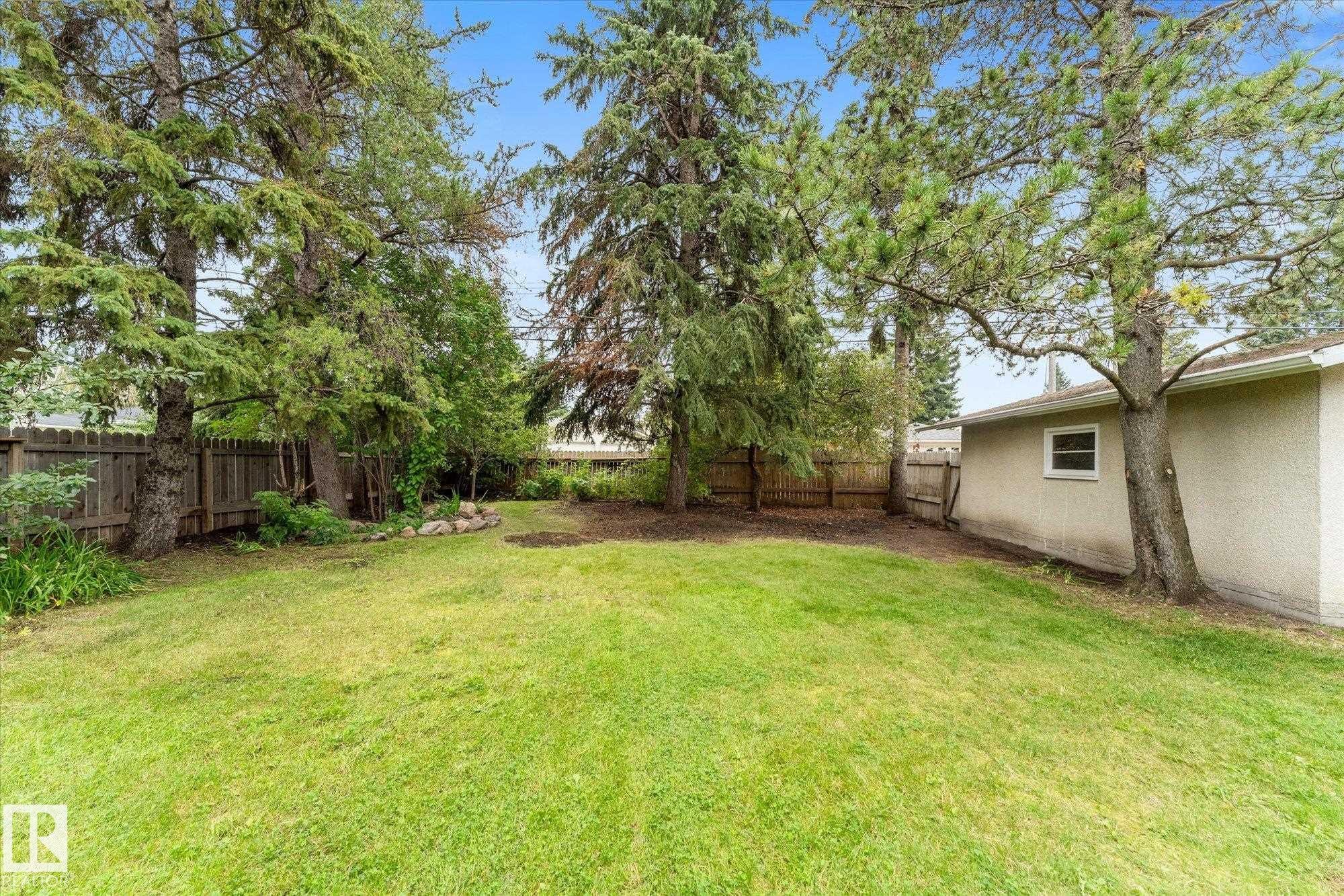 Expansive green lawn, mature trees, wood privacy fencing, and a stucco-sided exterior - 11311 Malmo Road Nw, Edmonton, AB