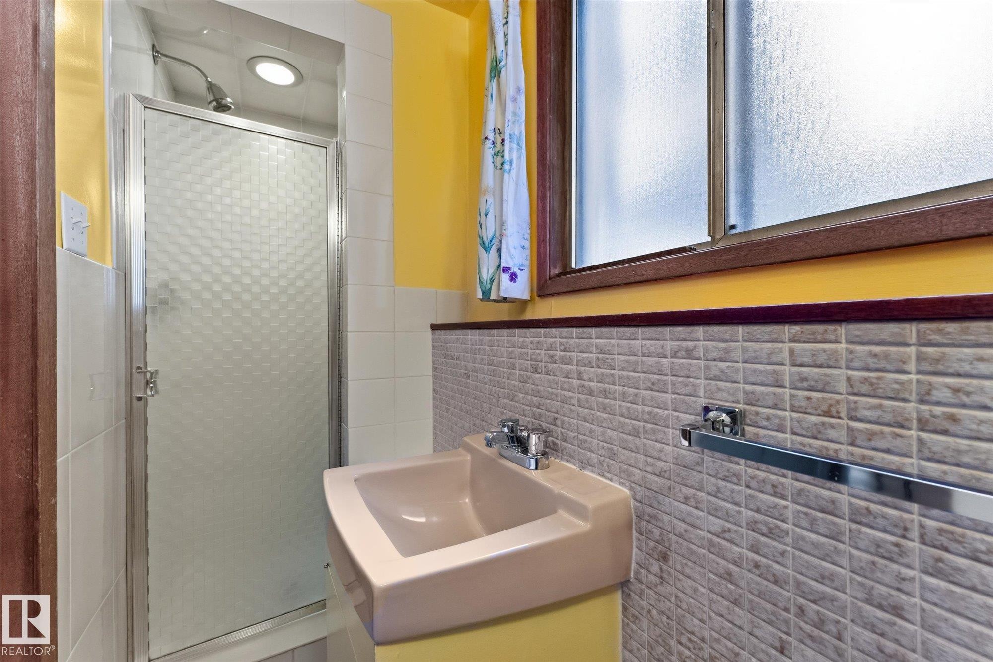 Wall-mounted sink with chrome fixtures, textured wall tiling, and a frosted window with a wood frame - 11311 Malmo Road Nw, Edmonton, AB