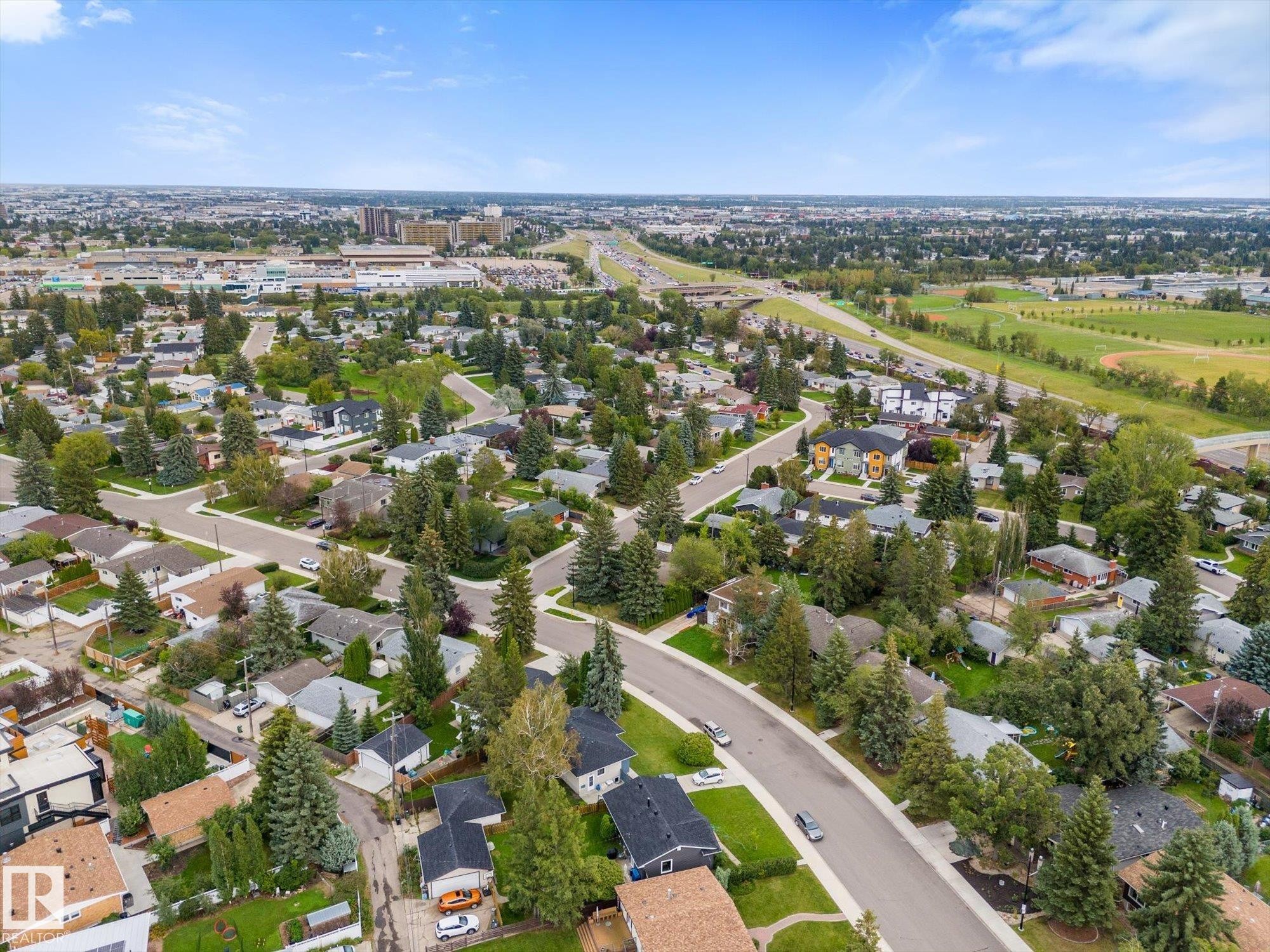 Established neighborhood with mature trees, residential street, curved roads, distant commercial buildings, and open green spaces - 11311 Malmo Road Nw, Edmonton, AB