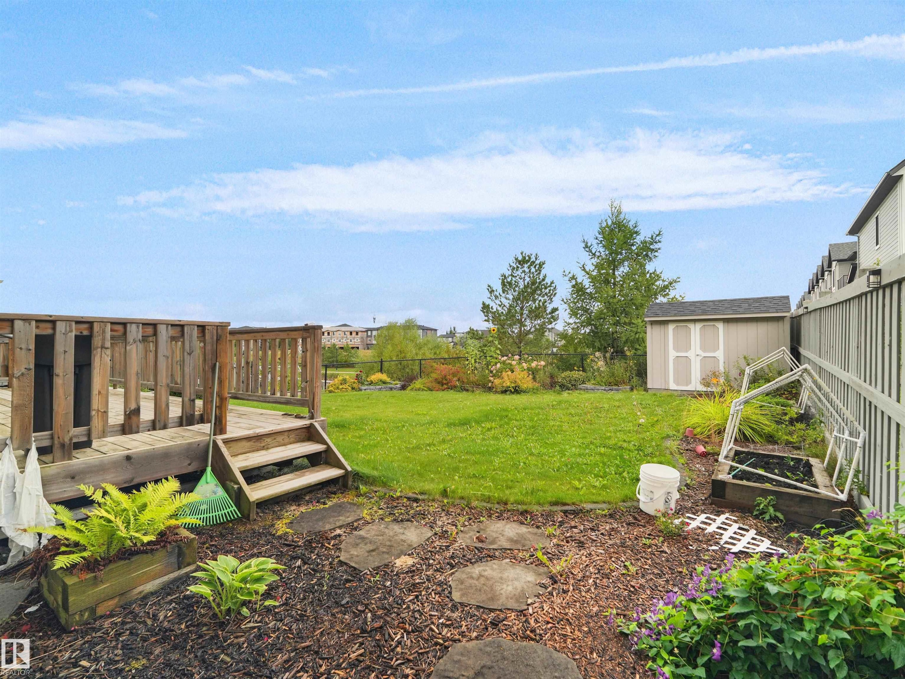 Expansive backyard featuring a wood deck with steps, a detached storage shed, a manicured lawn, and a planted garden bed - 6656 Cardinal Rd Sw, Edmonton, AB