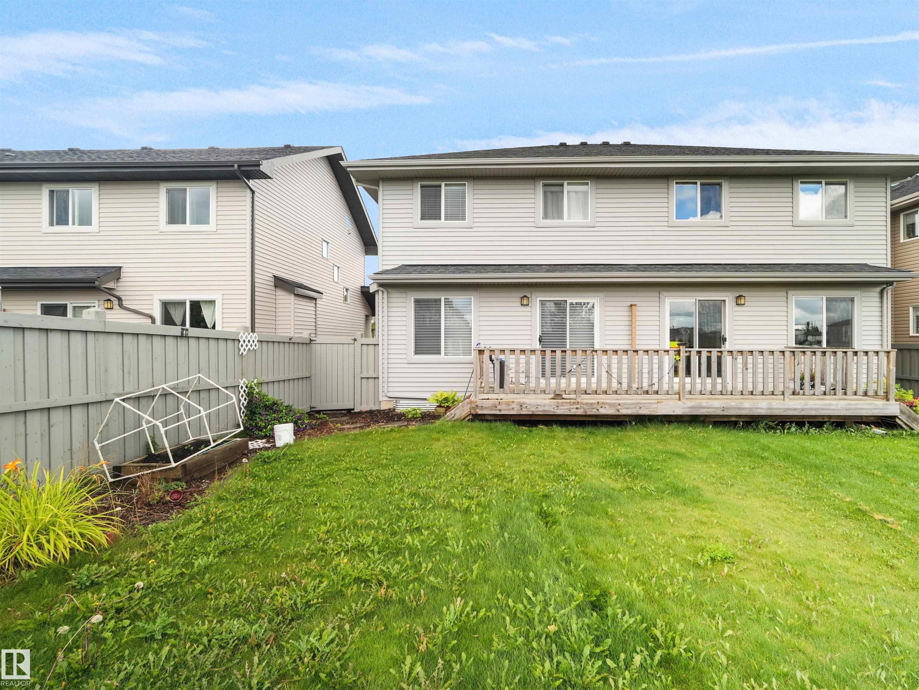Expansive backyard featuring a wood deck, sliding glass doors, and privacy fencing - 6656 Cardinal Rd Sw, Edmonton, AB