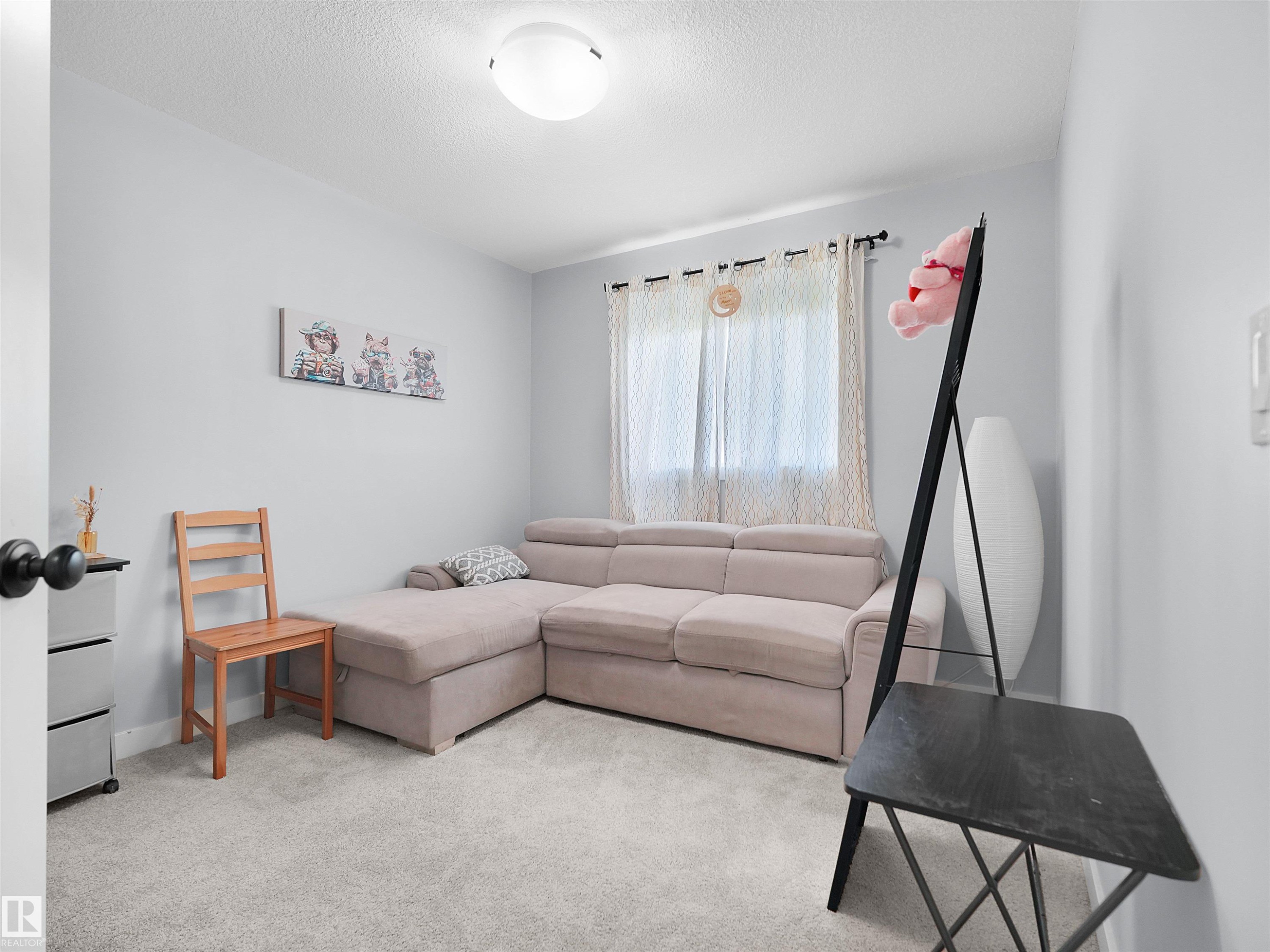 Carpeted room featuring light gray walls, a window with sheer curtains, and a flush mount ceiling light - 6656 Cardinal Rd Sw, Edmonton, AB