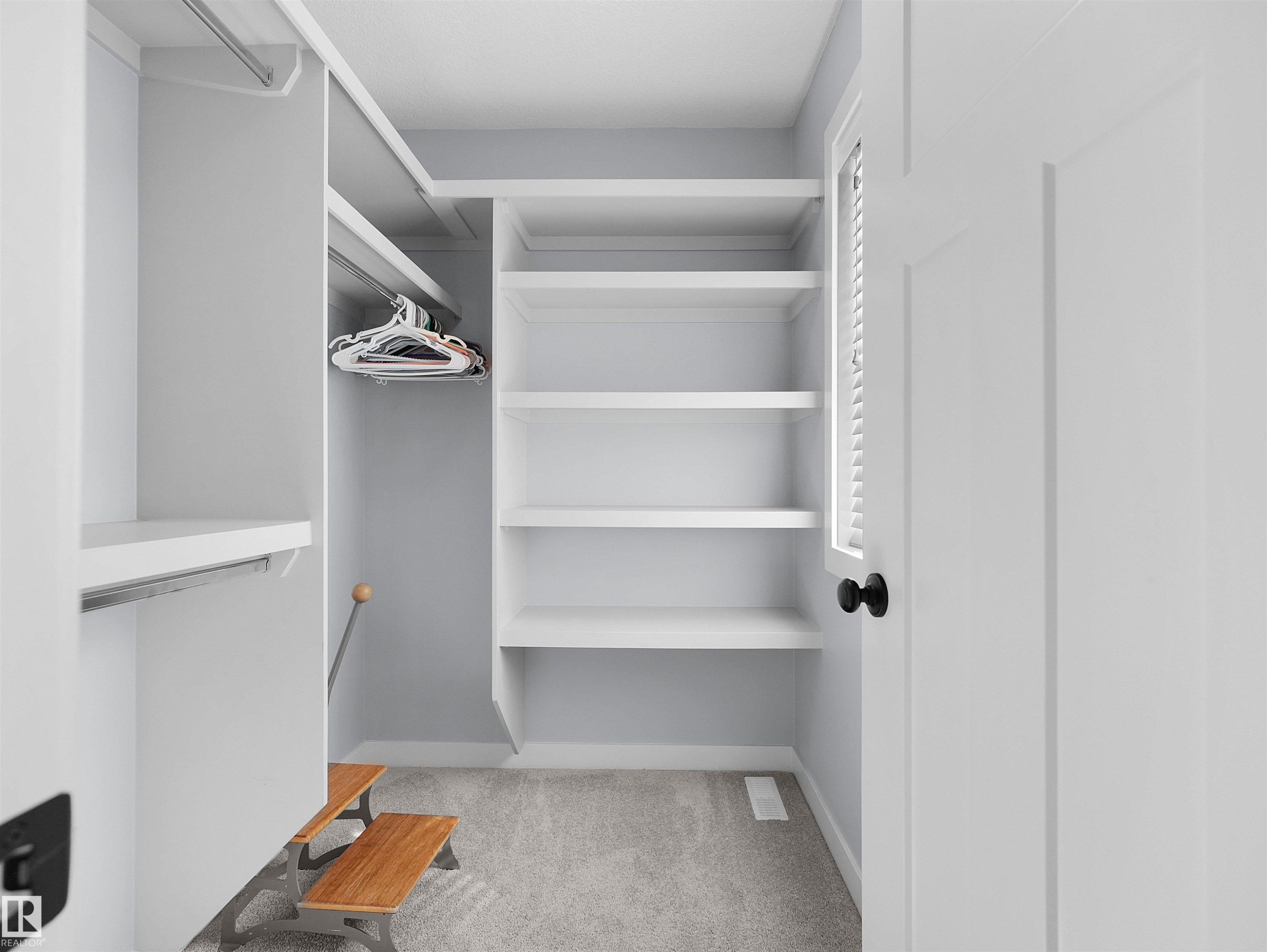 Custom closet system with built-in shelving, hanging rods, and light gray carpeting - 6656 Cardinal Rd Sw, Edmonton, AB