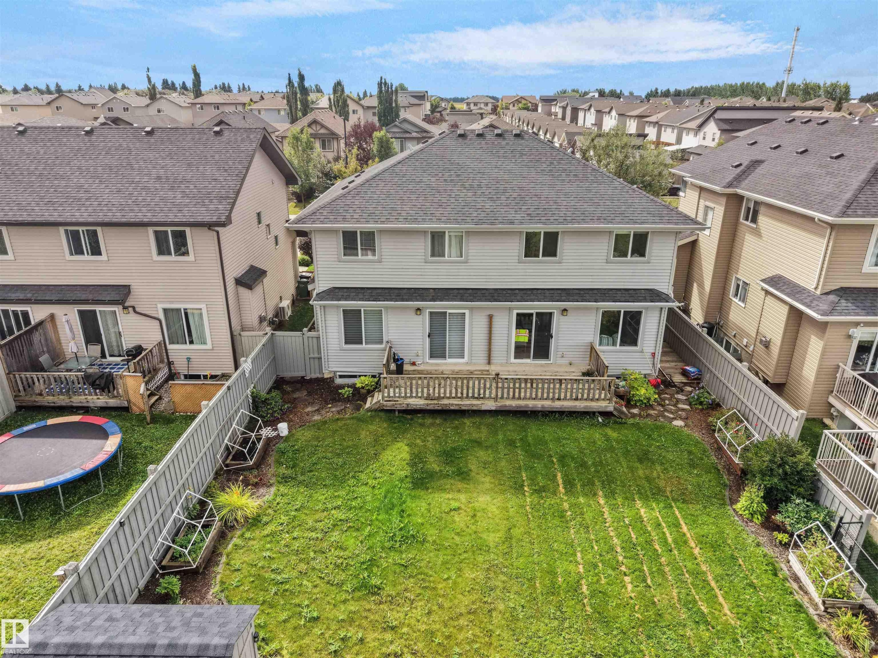 Expansive backyard featuring a manicured lawn, wood deck, and partial privacy fencing - 6656 Cardinal Rd Sw, Edmonton, AB