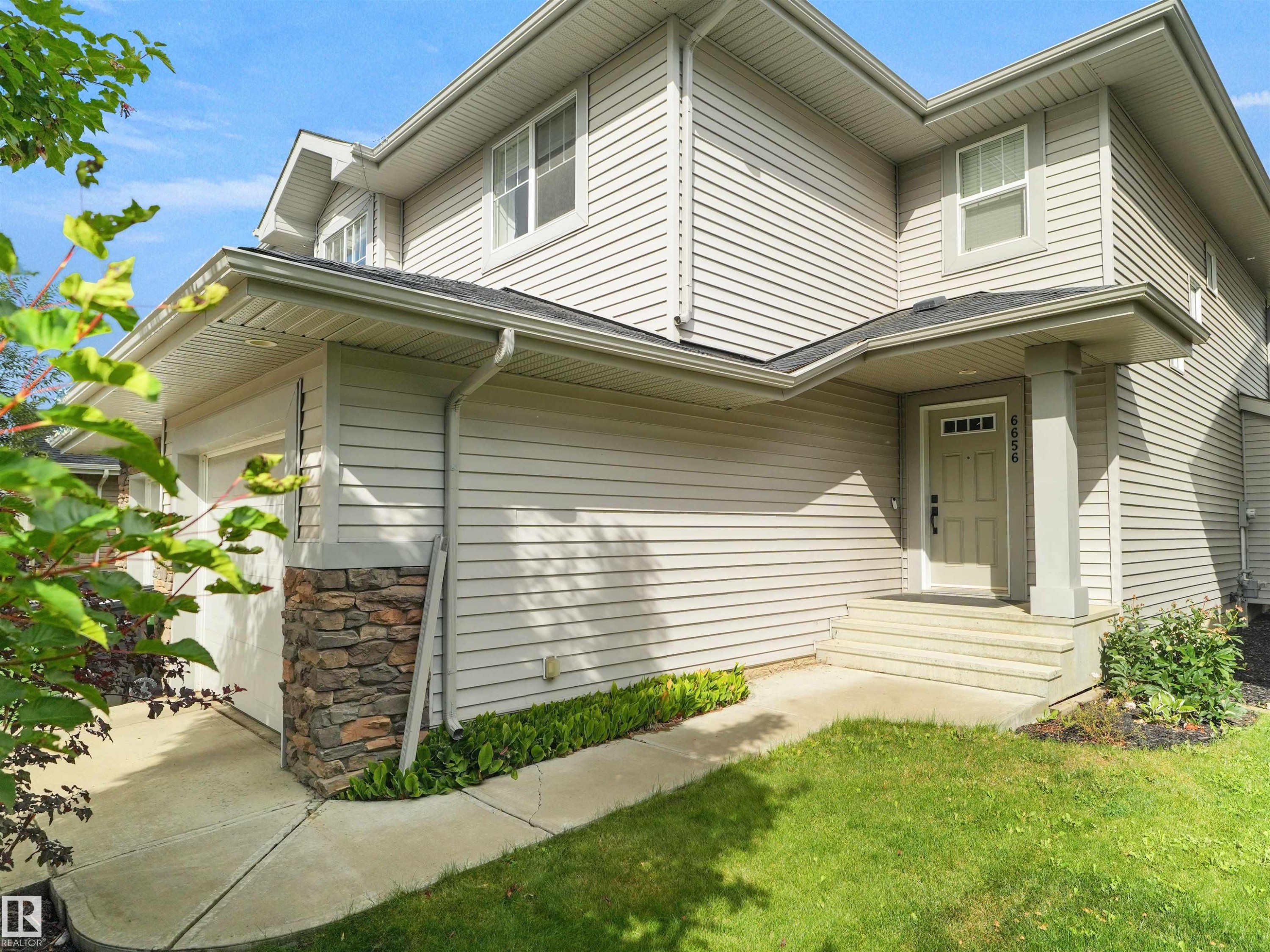 Light-toned siding exterior with stacked stone accents, covered entry, front door with transom window, and concrete entry steps - 6656 Cardinal Rd Sw, Edmonton, AB
