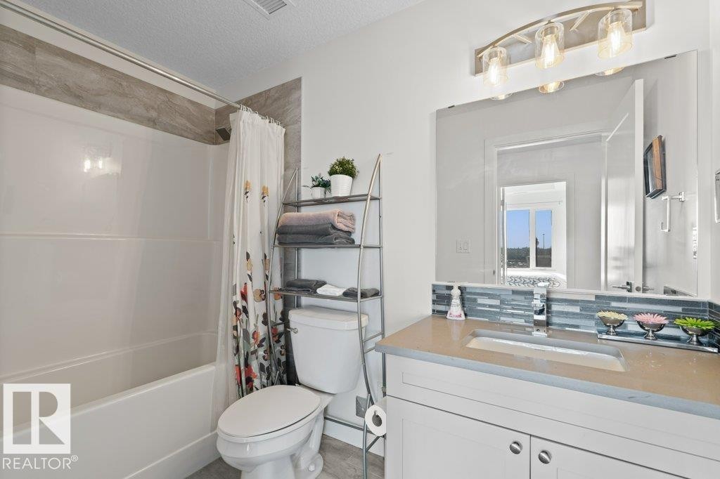 Bathroom featuring a combined tub and shower, a single vanity with a solid surface countertop, an integrated sink, and an extensive wall mirror - 1316 Windermere Way Sw, Edmonton, AB