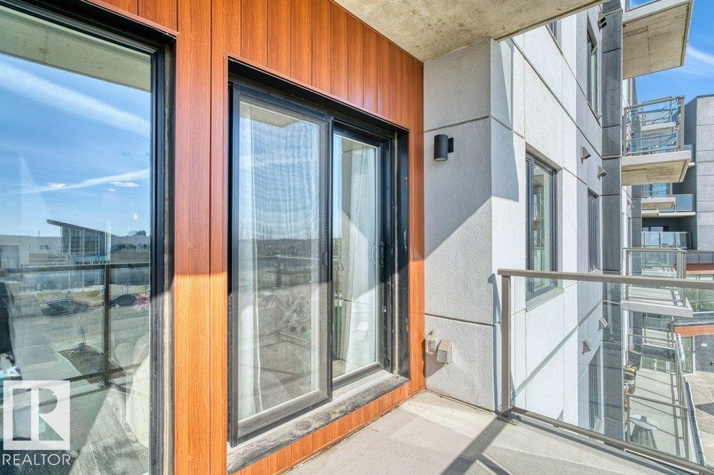 Private balcony with glass railing, featuring wood-look paneling, concrete flooring, and black-framed sliding glass doors - 1316 Windermere Way Sw, Edmonton, AB