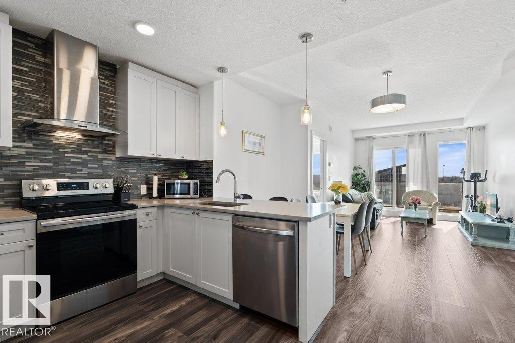 Contemporary kitchen featuring white cabinetry, stainless steel appliances, a tile backsplash, and a breakfast bar - 1316 Windermere Way Sw, Edmonton, AB