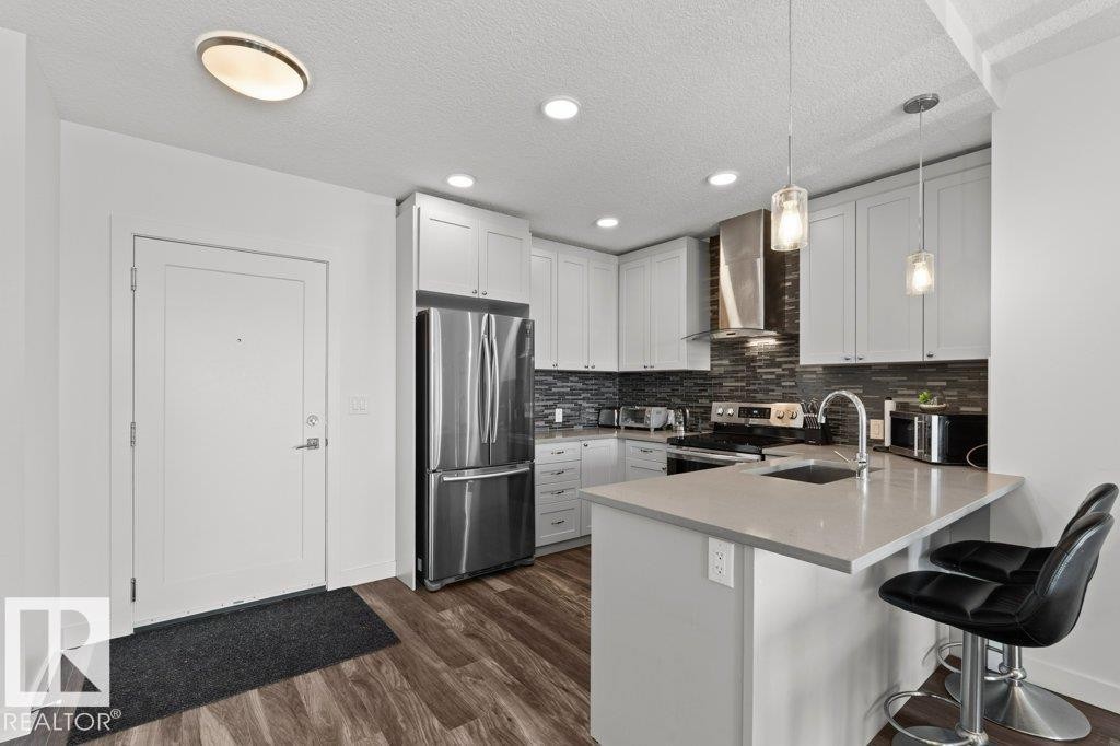 Modern kitchen featuring light cabinetry, stainless steel appliances, a dark tile backsplash, and light countertops with an integrated sink - 1316 Windermere Way Sw, Edmonton, AB