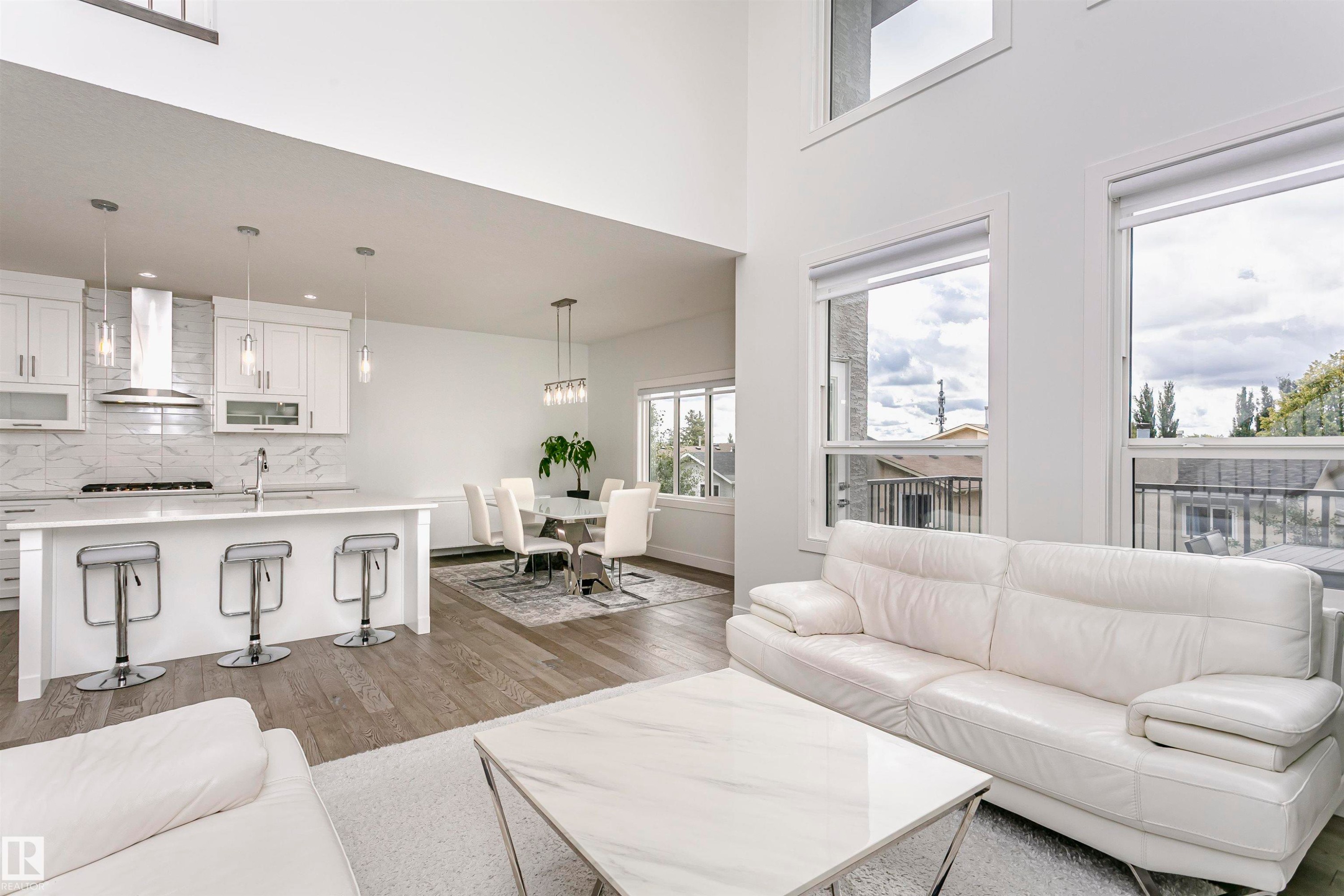 Vaulted ceilings, wood-finish flooring, white cabinetry, a kitchen island with seating, and large windows - 9107 181 Avenue Nw, Edmonton, AB