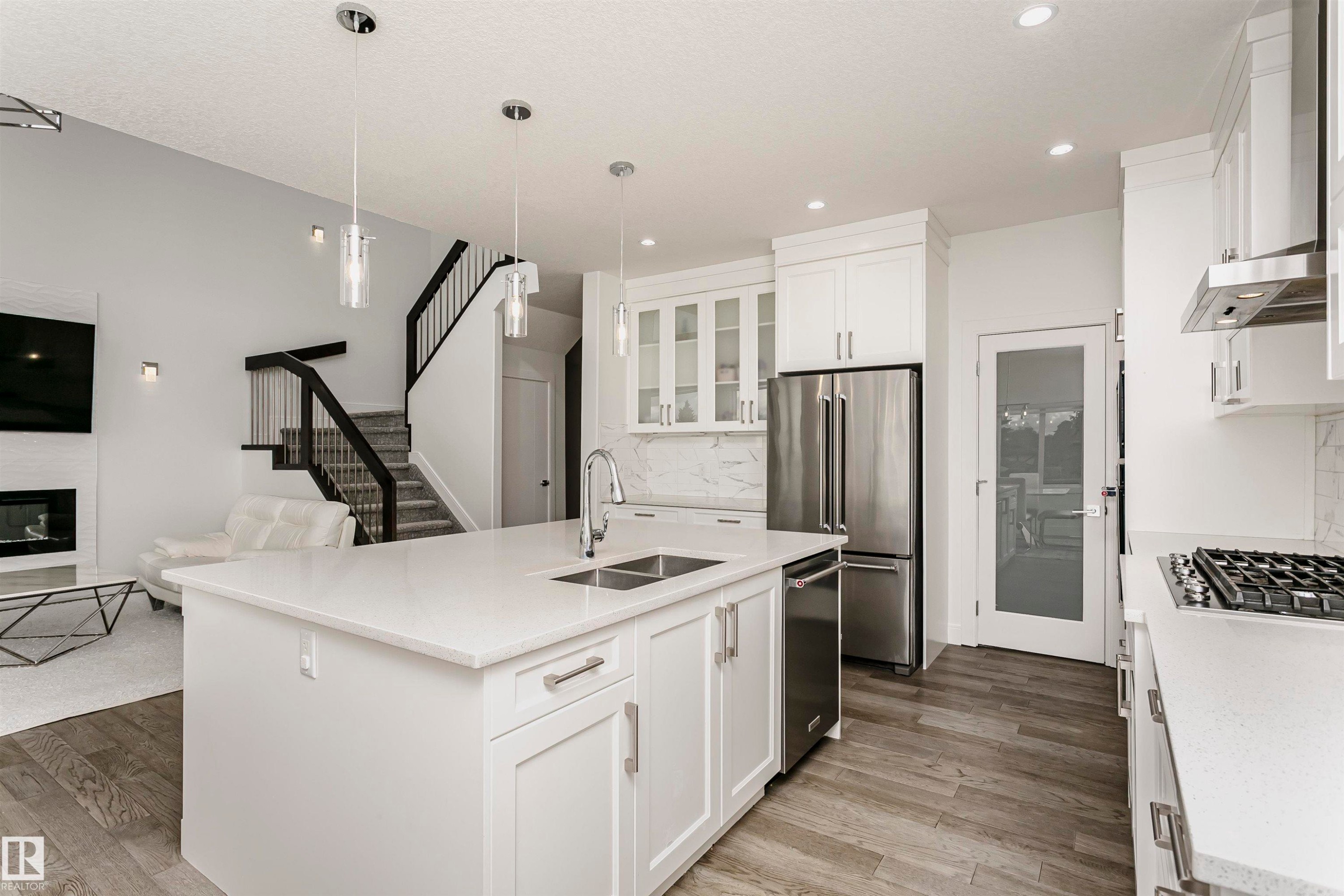 Open-concept kitchen featuring an island with a double sink, stainless steel appliances, white cabinetry, and wood-finish flooring - 9107 181 Avenue Nw, Edmonton, AB