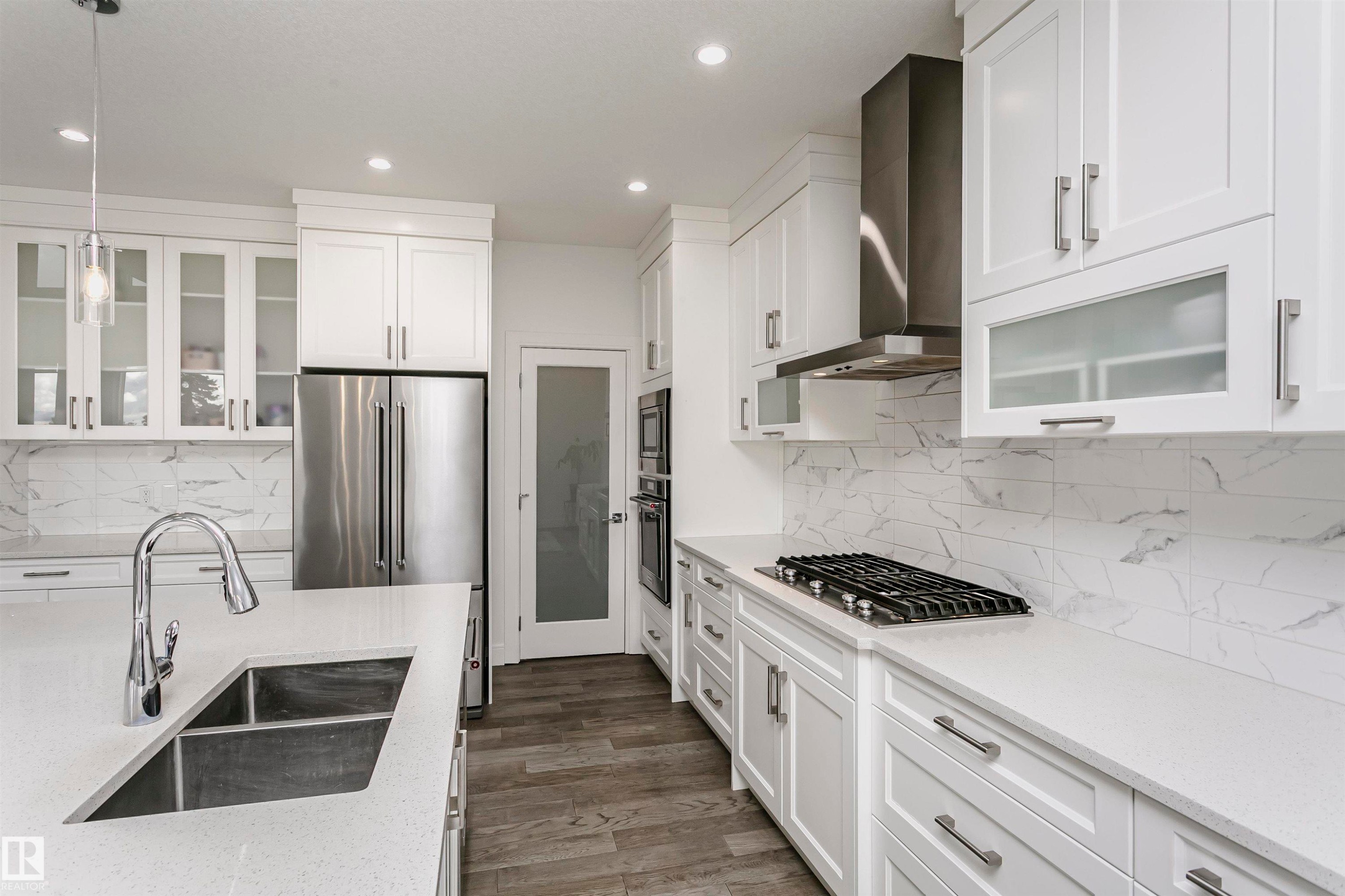 White shaker-style cabinetry with chrome hardware, integrated stainless steel appliances, white countertops, and full-height backsplash - 9107 181 Avenue Nw, Edmonton, AB