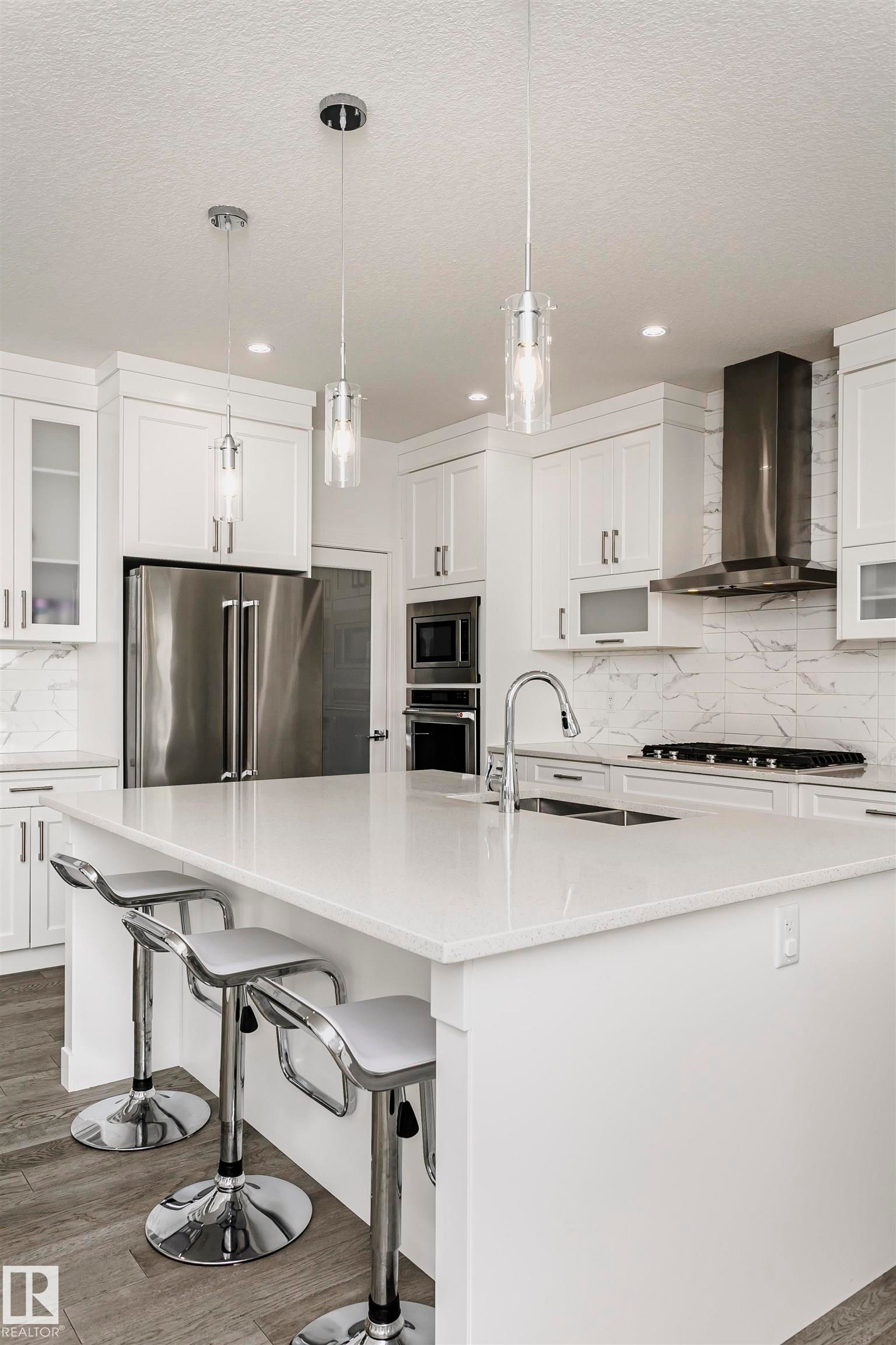 White cabinetry with integrated stainless steel appliances and a white stone countertop island - 9107 181 Avenue Nw, Edmonton, AB