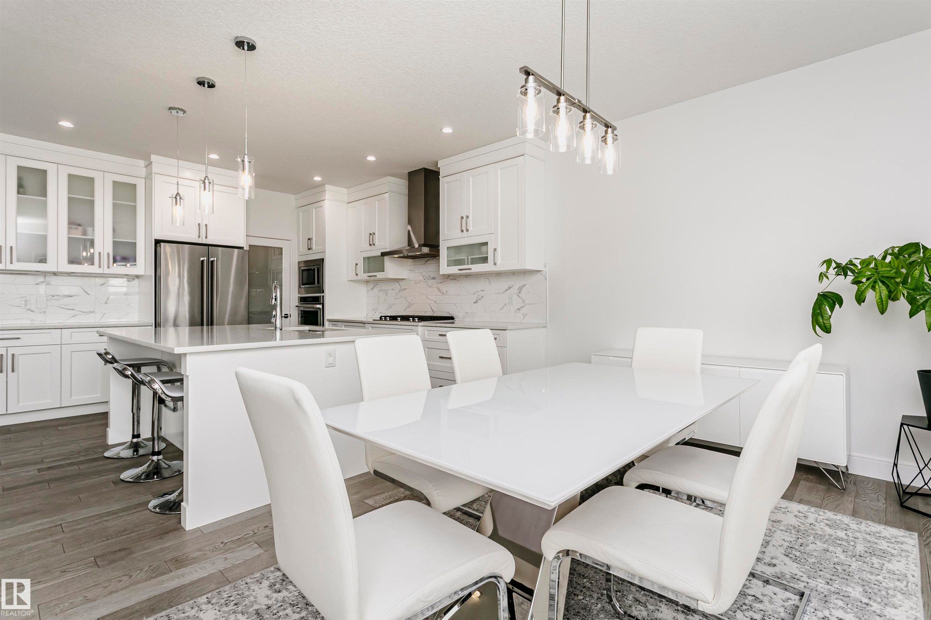 Modern kitchen and dining area featuring recessed lighting, stainless steel appliances, white cabinetry, a kitchen island with seating, and wood-finish flooring - 9107 181 Avenue Nw, Edmonton, AB