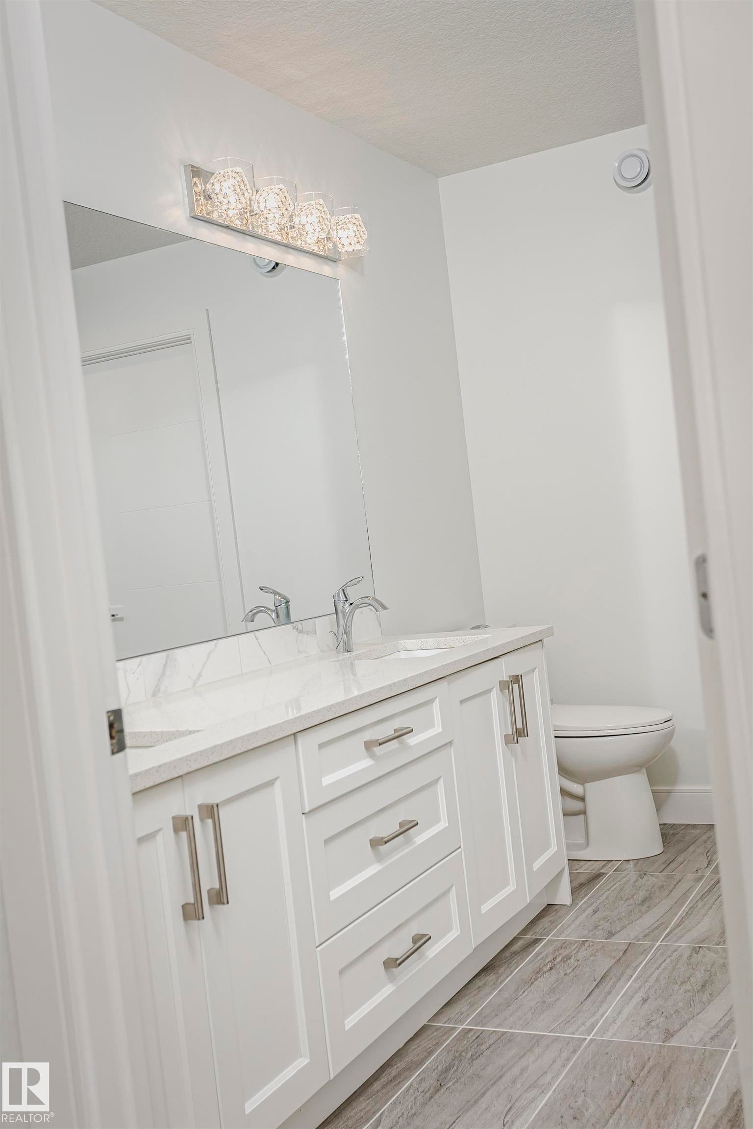 Dual vanity with white shaker-style cabinetry, undermount sinks, and a stone countertop - 9107 181 Avenue Nw, Edmonton, AB