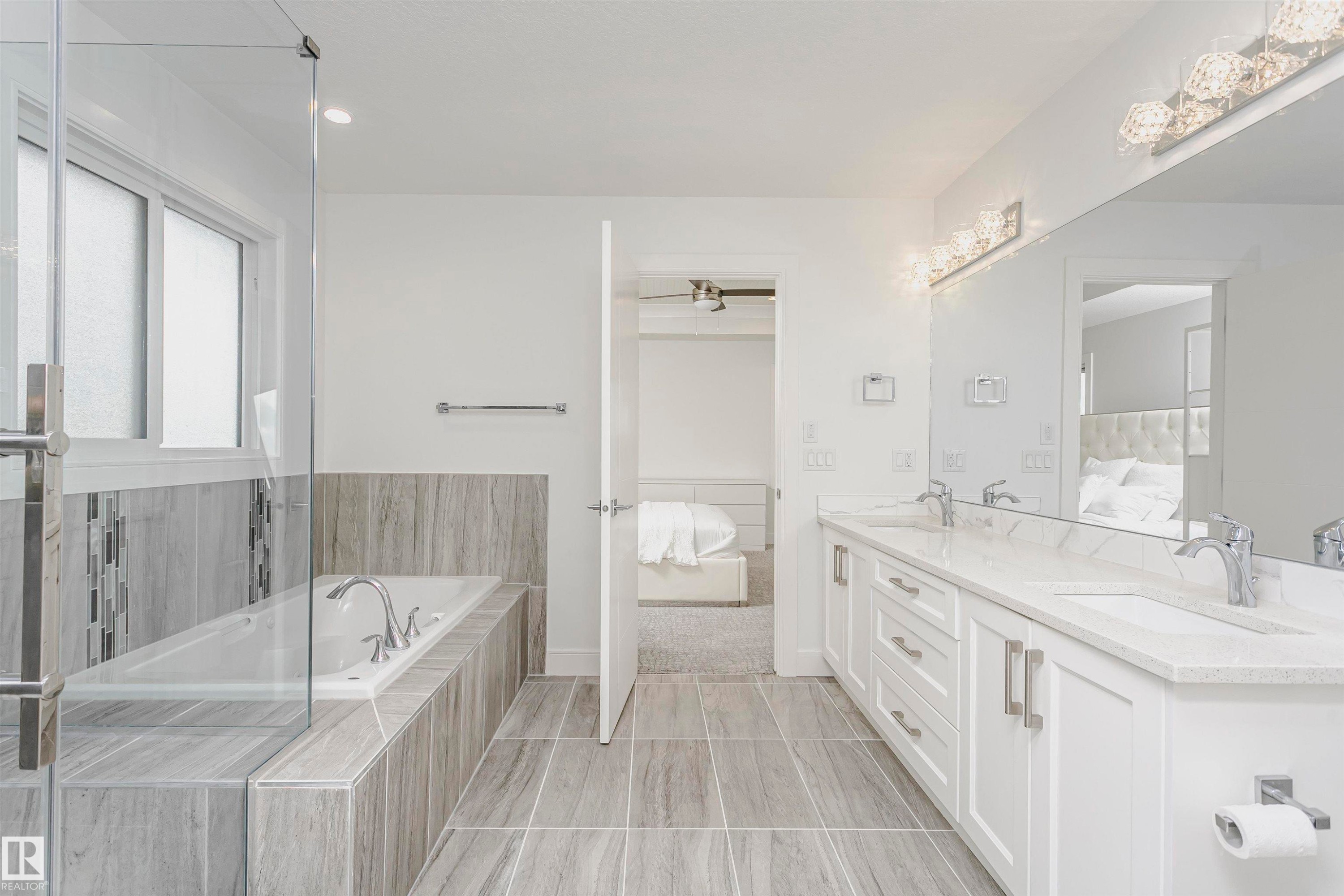 Dual vanity with stone countertops and undermount sinks, glass-enclosed shower, soaking tub, and tile flooring - 9107 181 Avenue Nw, Edmonton, AB