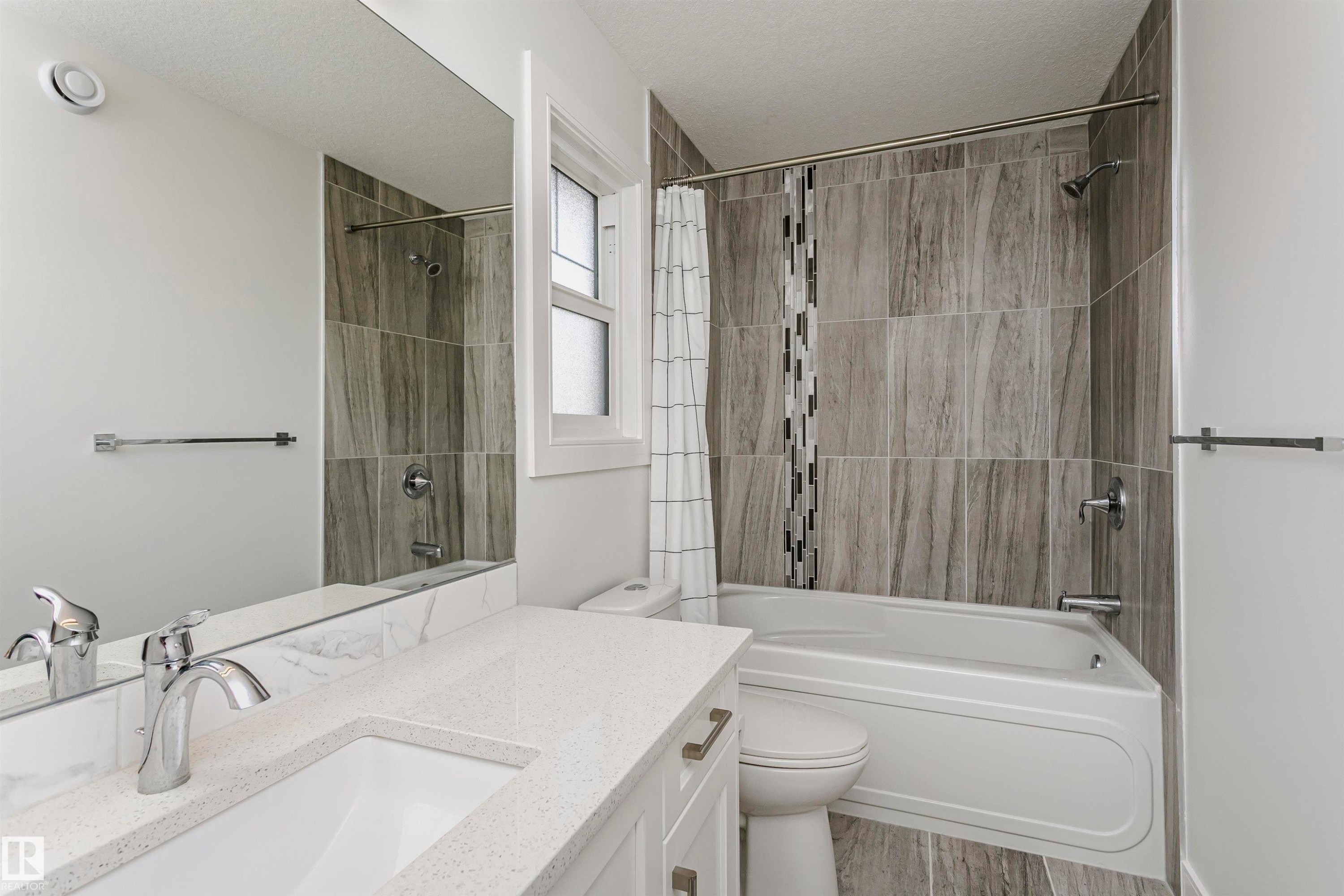 White vanity with a quartz countertop and integrated sink, polished chrome faucet, and full-width mirror - 9107 181 Avenue Nw, Edmonton, AB