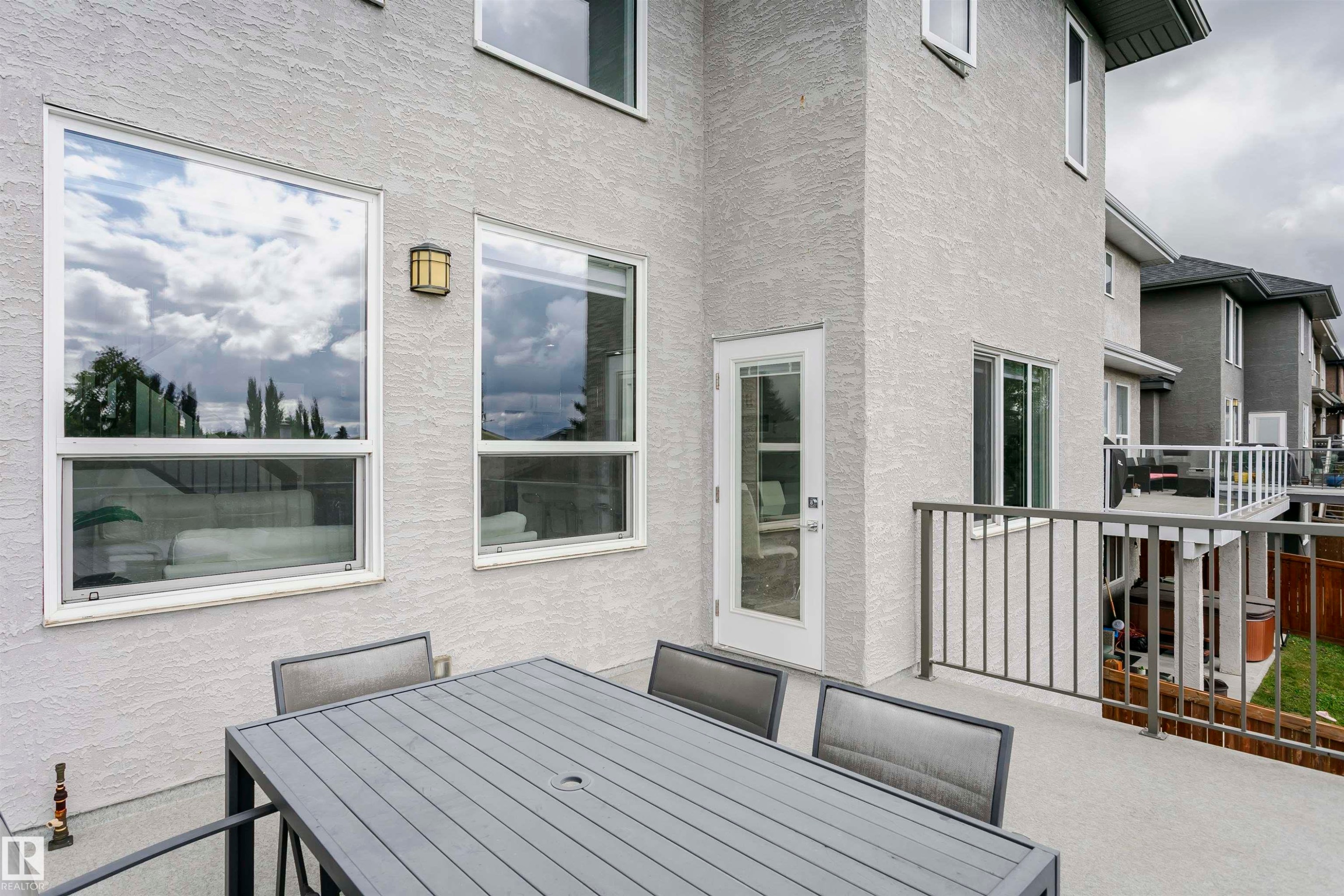 Exterior stucco finish, multiple large windows, glass-paneled door, and a deck with metal railings - 9107 181 Avenue Nw, Edmonton, AB