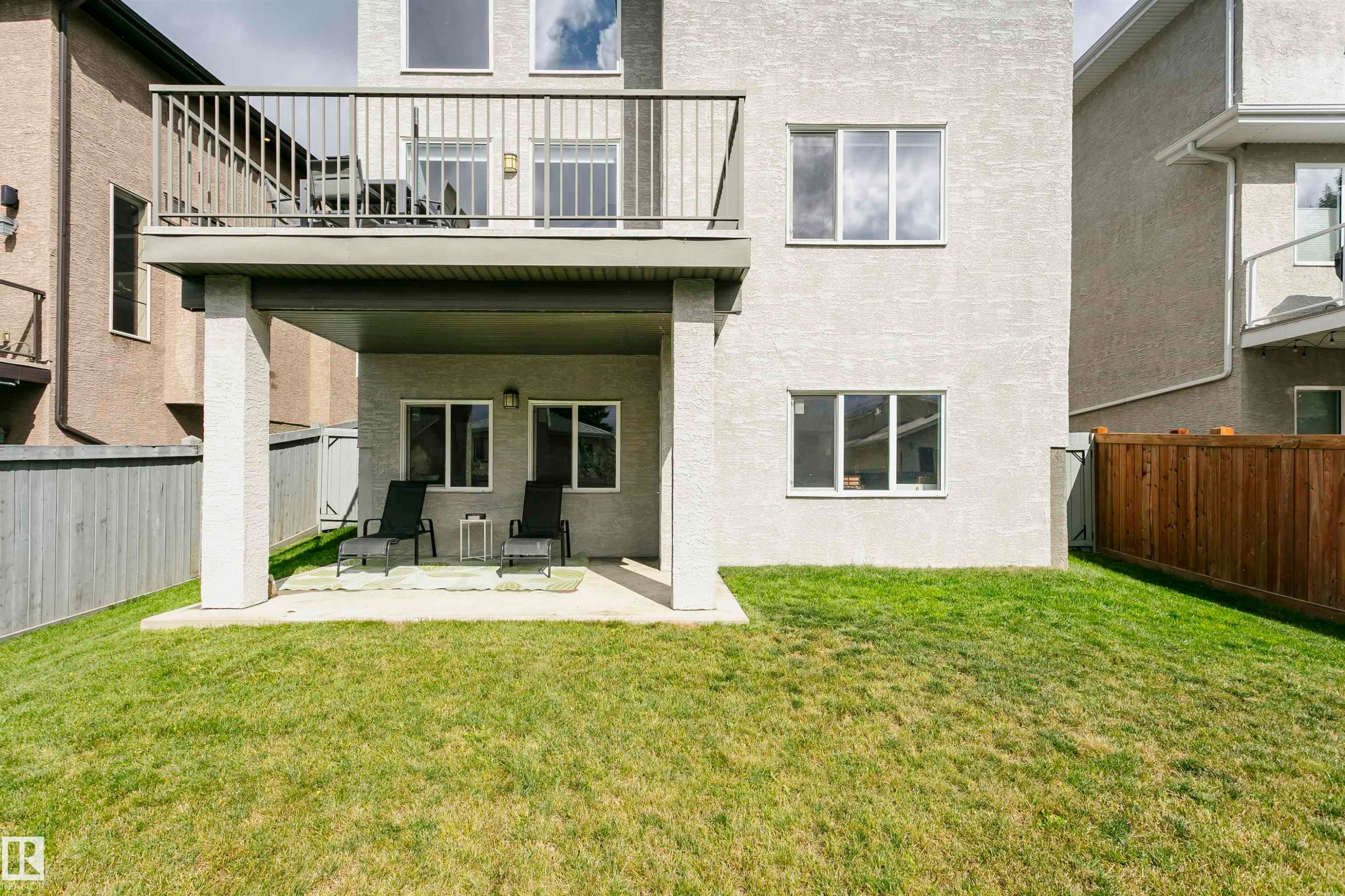 Rear exterior featuring a ground-level patio, upper-level balcony with metal railing, and a fenced yard - 9107 181 Avenue Nw, Edmonton, AB