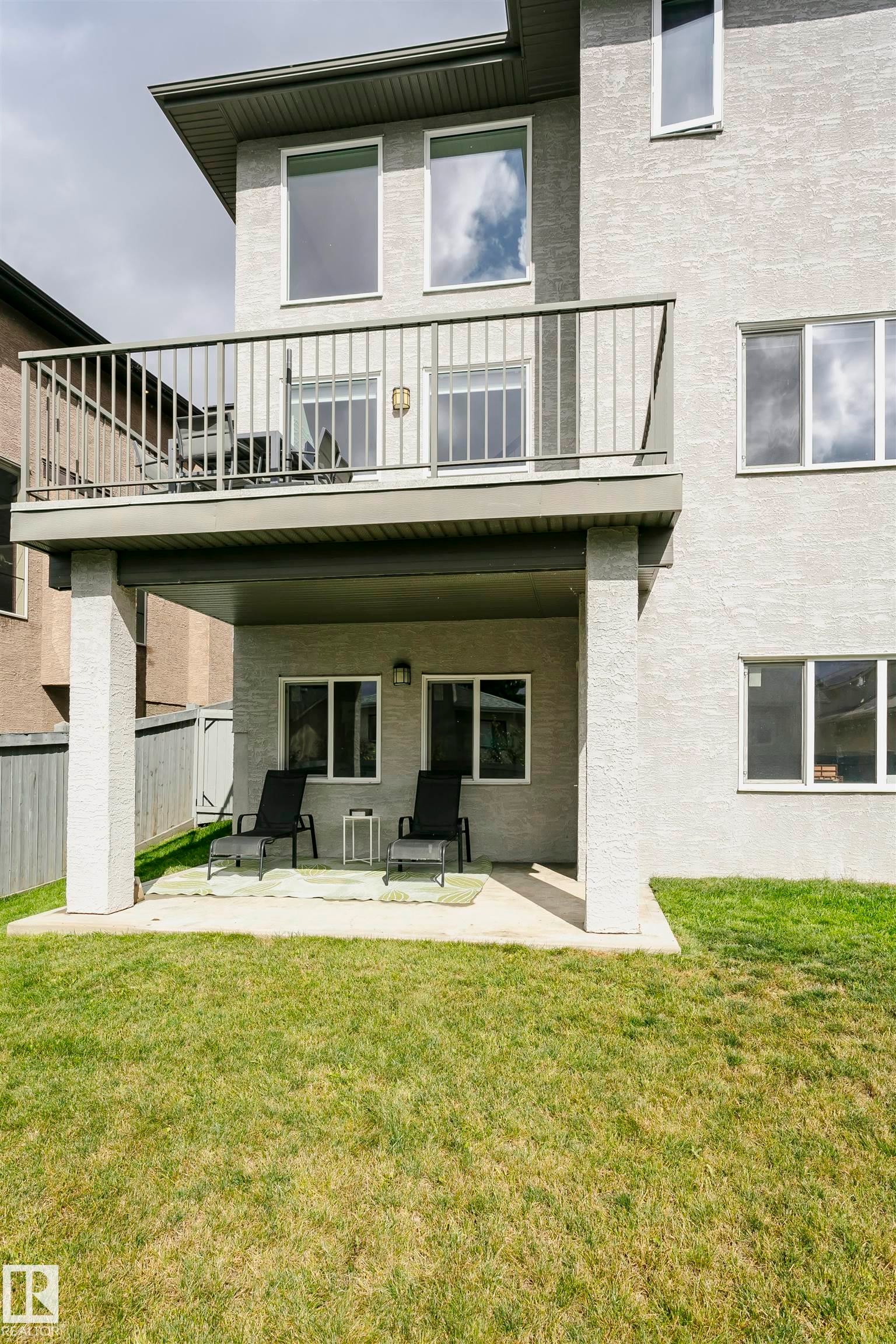 Upper-level balcony with metal railing, lower-level patio, and a manicured grass yard - 9107 181 Avenue Nw, Edmonton, AB