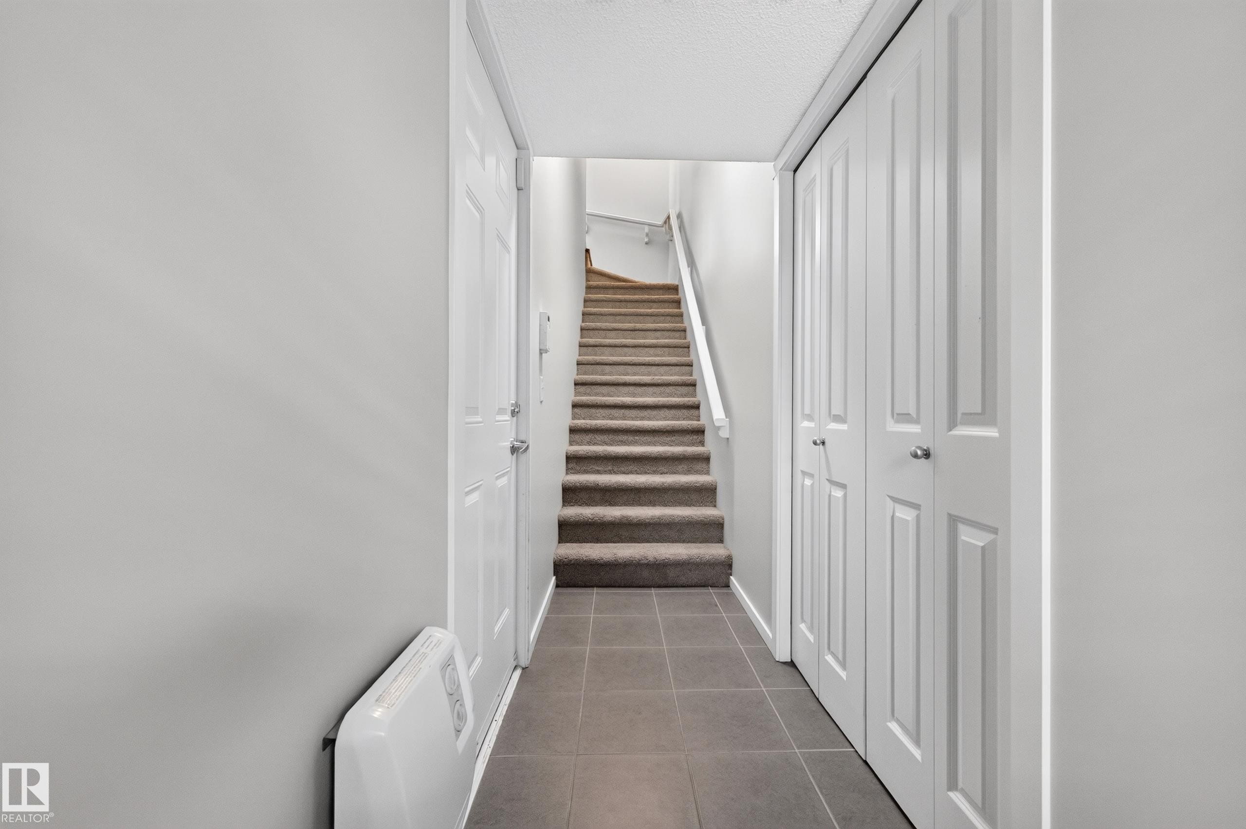 Hallway from garage to second floor featuring tiled flooring, carpeted staircase, paneled interior doors, and bi-fold closet doors - #72 603 Watt Bv Sw Sw, Edmonton, AB