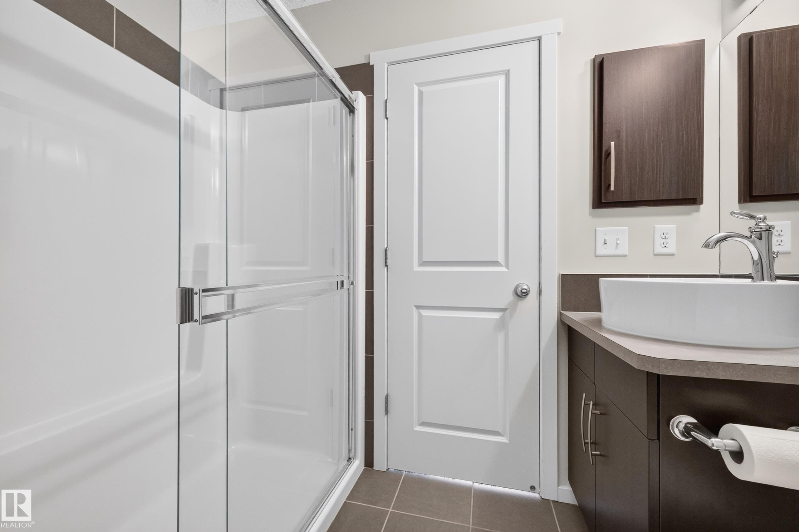Glass-enclosed shower with white surround, brown tiled floor, dark wood-finish vanity with countertop, vessel sink, and chrome faucet - #72 603 Watt Bv Sw Sw, Edmonton, AB
