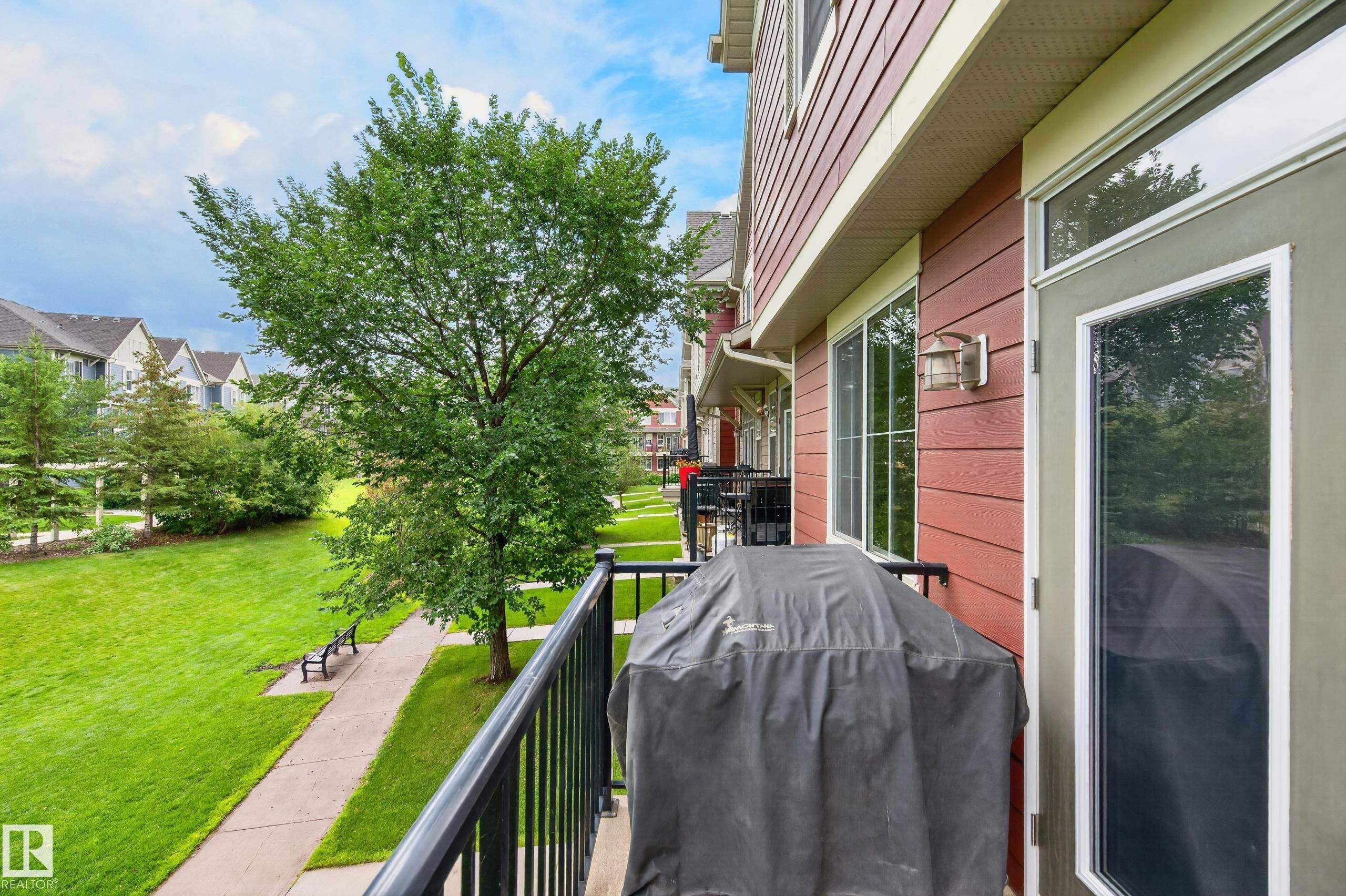 Exterior balcony with black metal railing, red horizontal siding, a glass-paneled door, and adjacent windows - #72 603 Watt Bv Sw Sw, Edmonton, AB