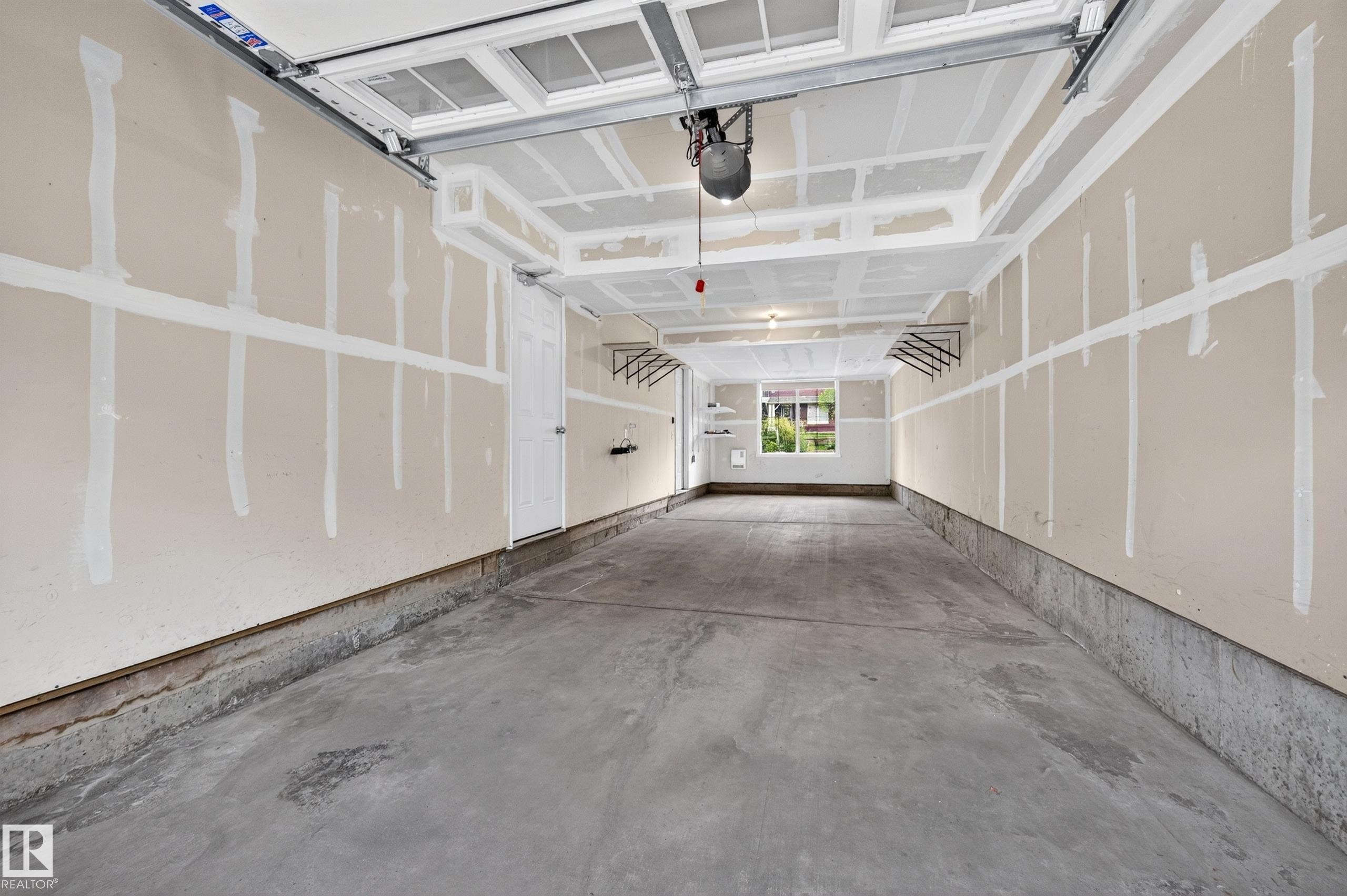 Spacious garage featuring a concrete floor, built-in shelving, a window, and an interior access door - #72 603 Watt Bv Sw Sw, Edmonton, AB
