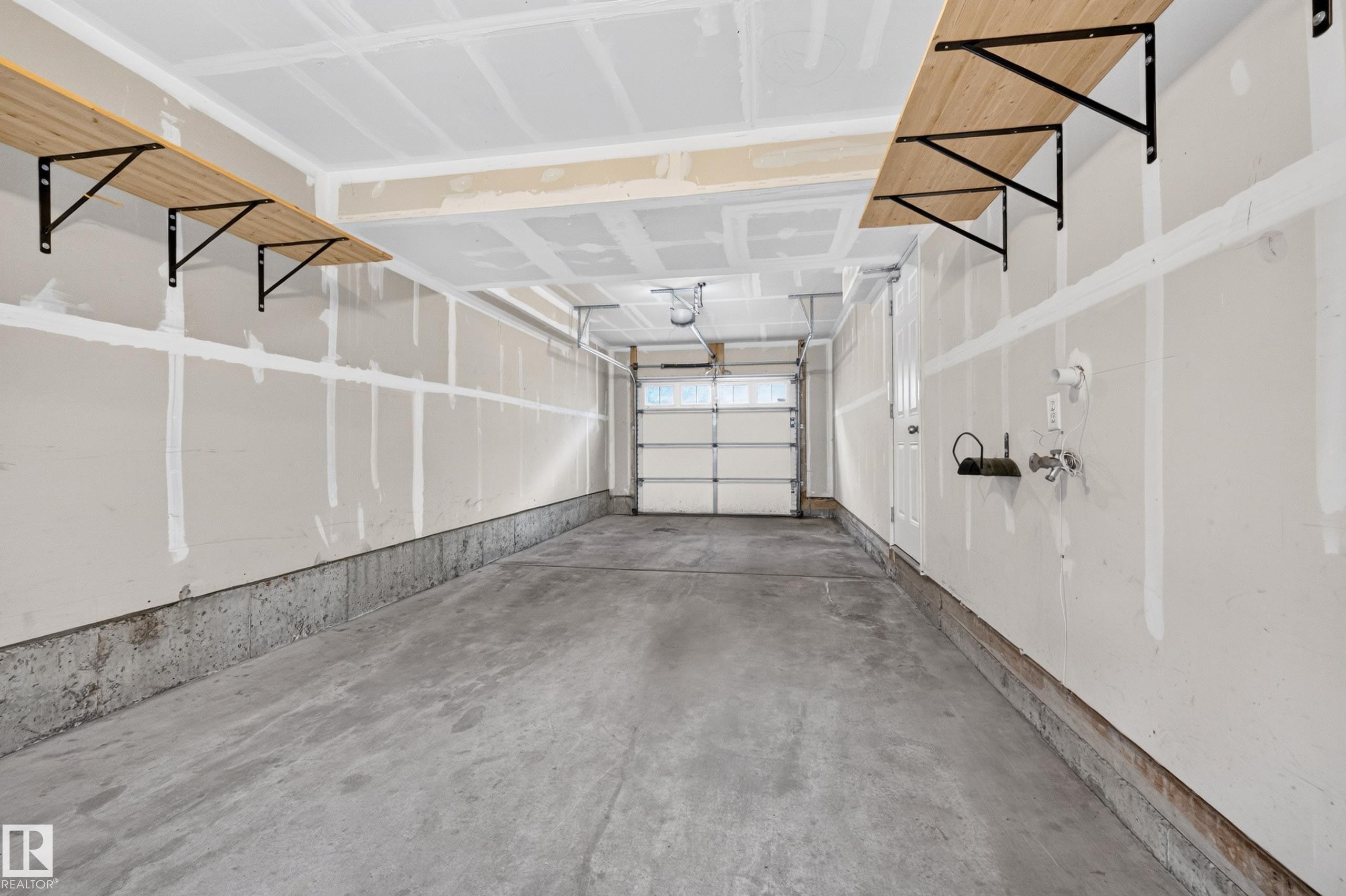 Two wall-mounted shelving units, concrete flooring, and an overhead garage door - #72 603 Watt Bv Sw Sw, Edmonton, AB
