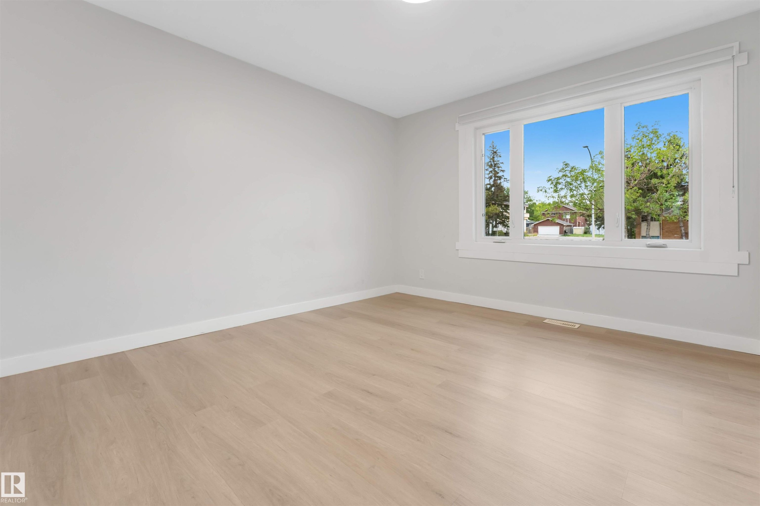 Light-toned wood-finish flooring, white trim, and a large window with three panes - 7928 82 Avenue Nw, Edmonton, AB