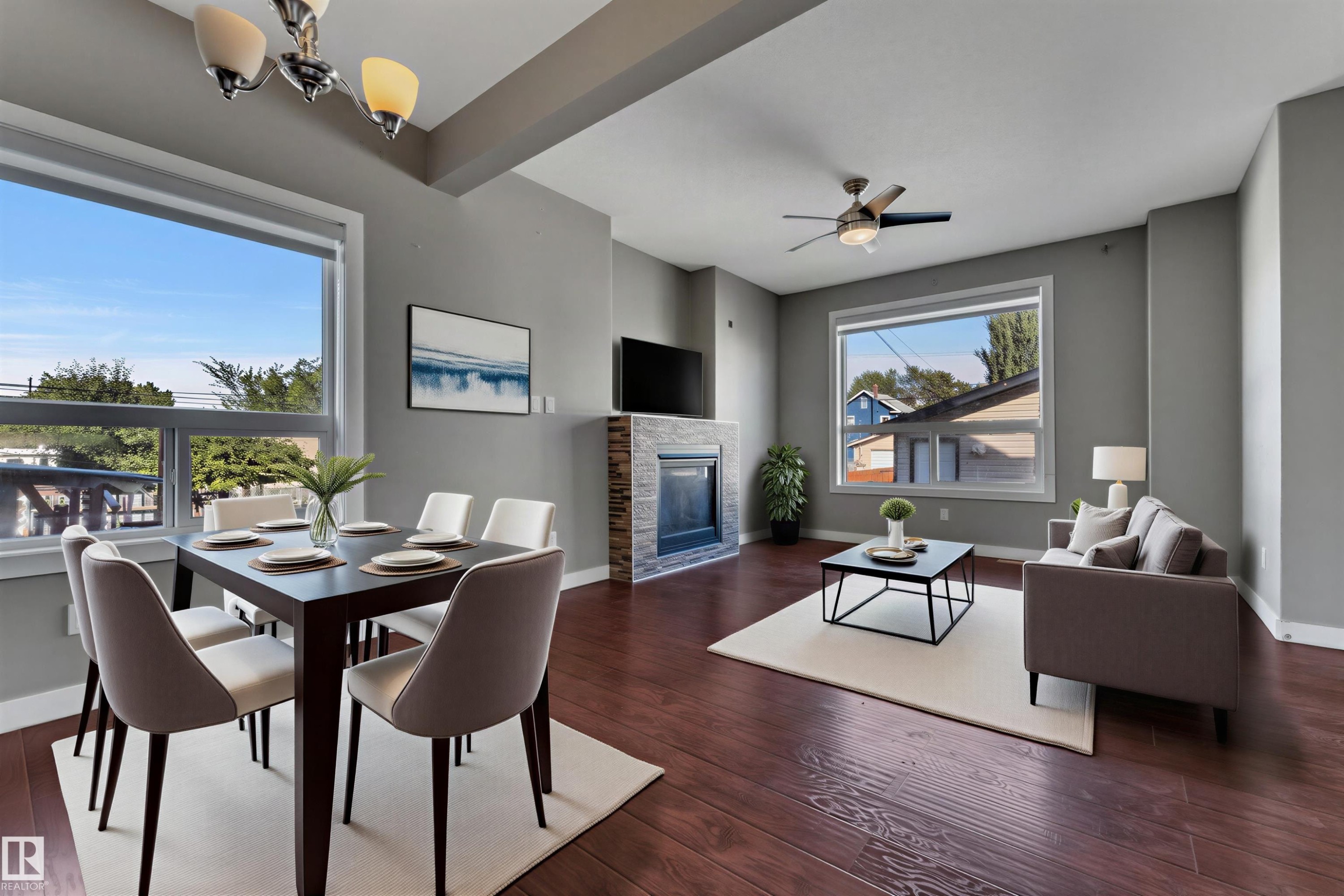 Open-concept living area featuring rich wood-finish flooring, a contemporary fireplace with a stone surround, and abundant natural light from large windows - 11421 82 Street Nw, Edmonton, AB